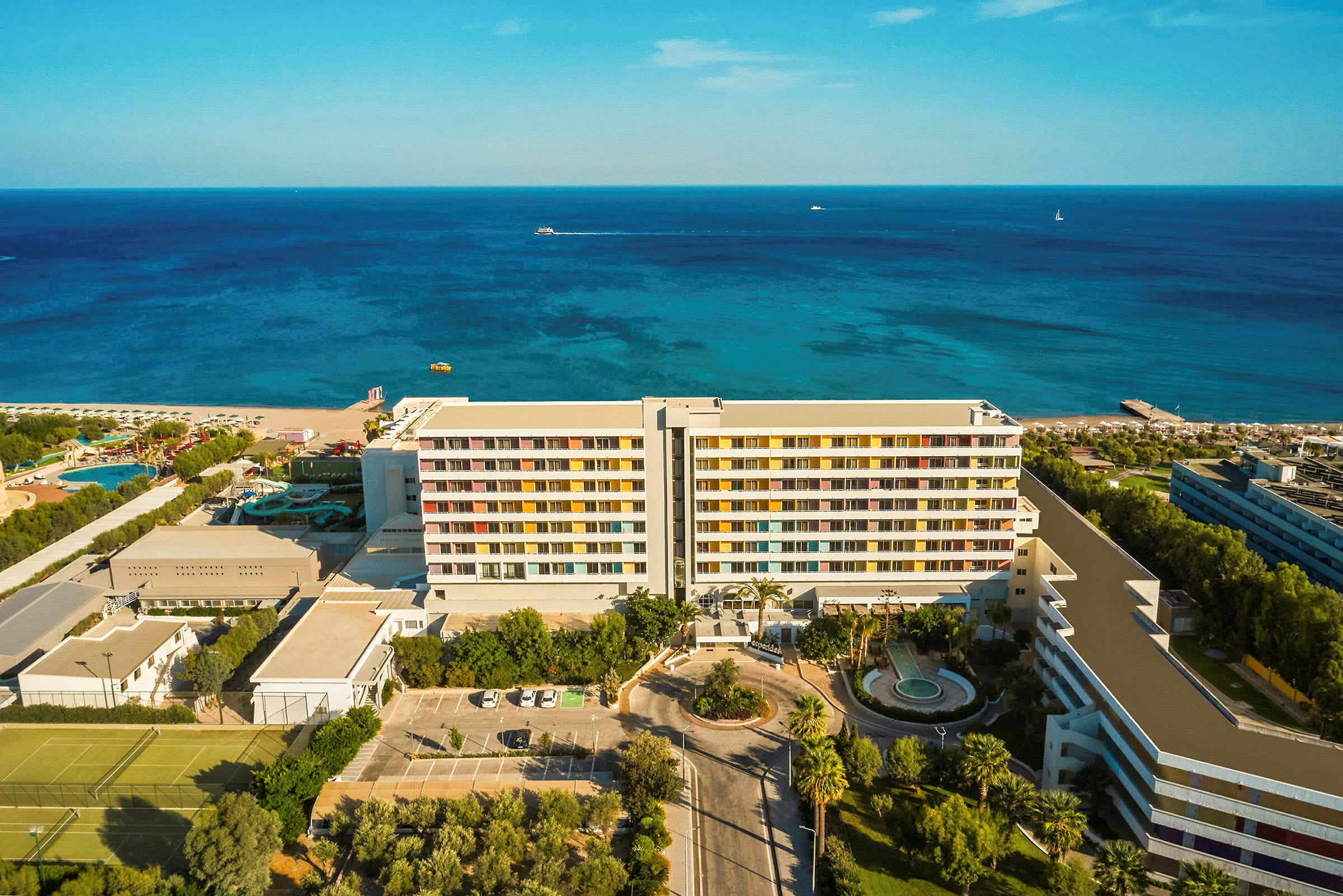 Flyutsikt av et hotell ved kysten med hav og strand i bakgrunnen. (AI-generert tekst)