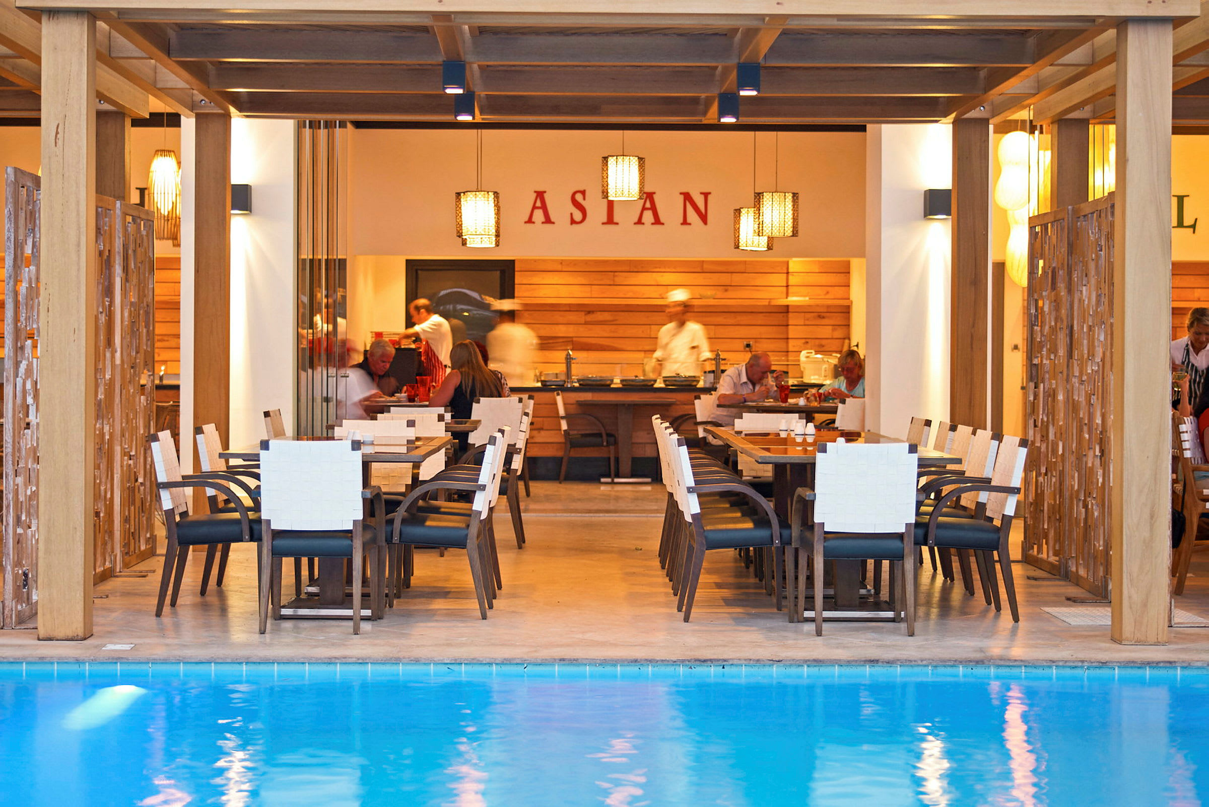 Restaurant ved et basseng med bord og stoler foran en matservering. (AI-generert tekst)