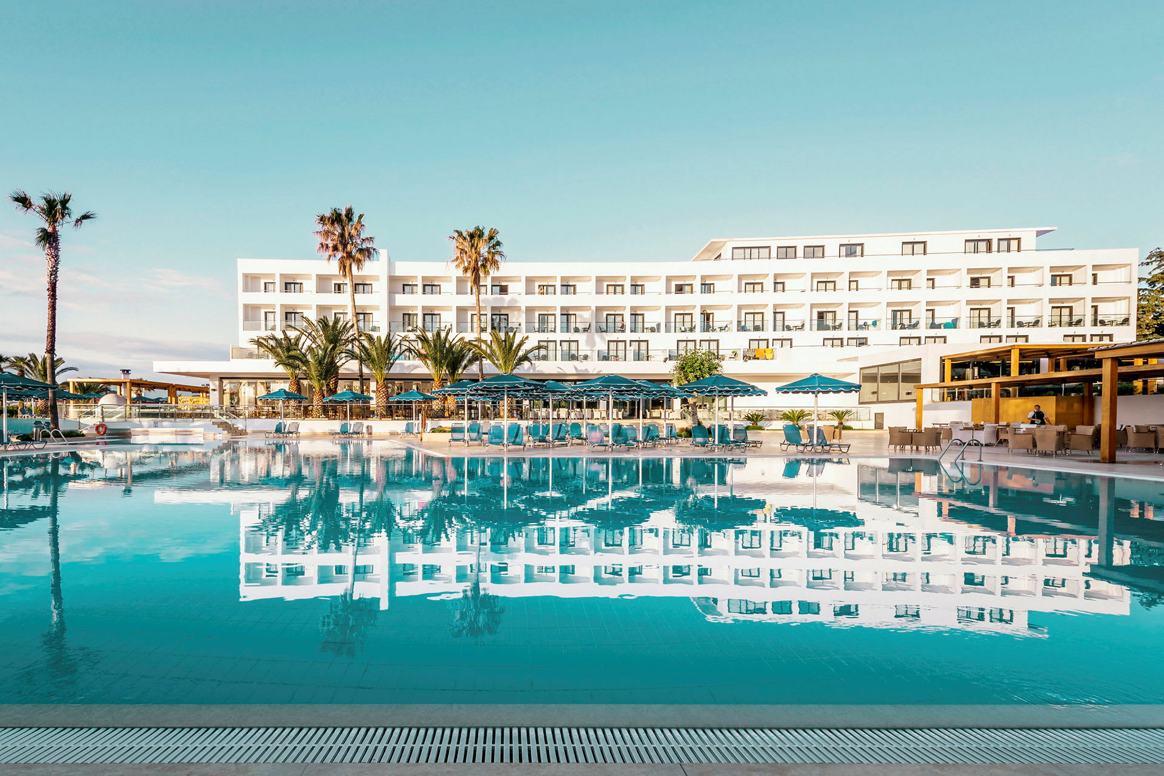 Hotellbygning med basseng og solsenger i forgrunnen. (AI-generert tekst)