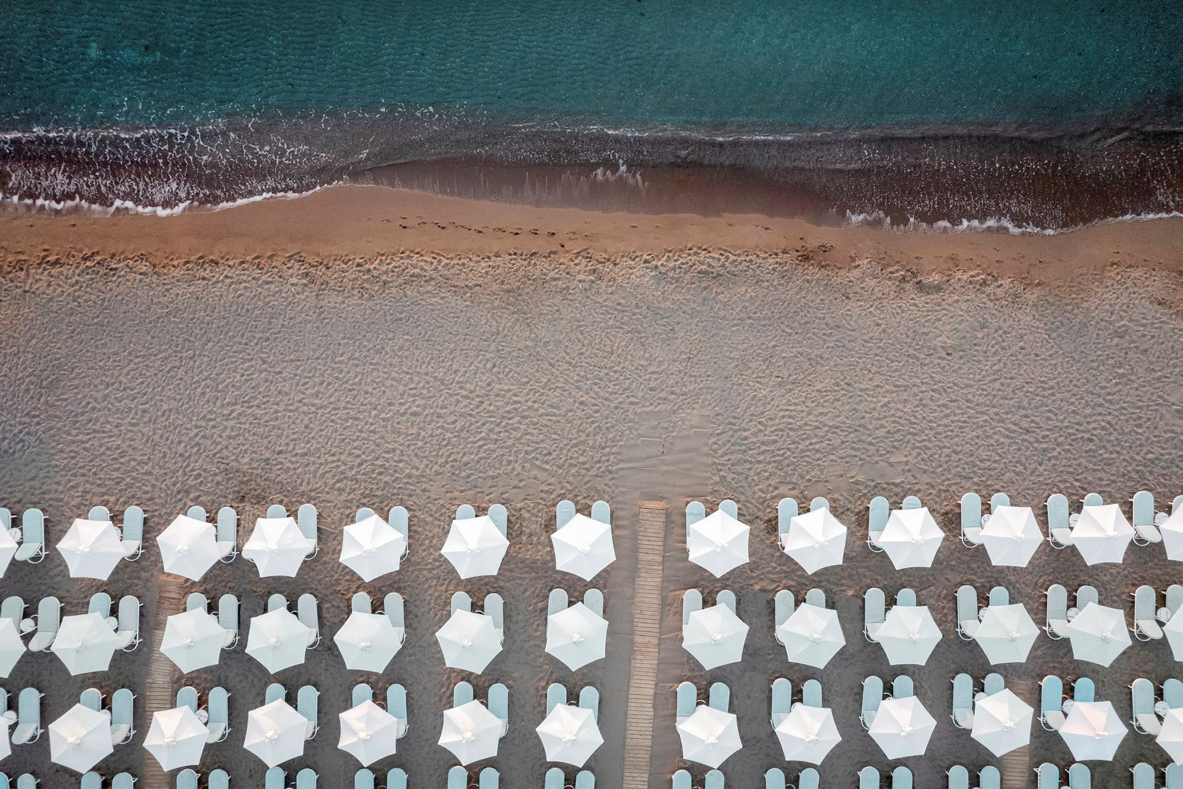 Fugleperspektiv av strand med hvite parasoller og solsenger ved kanten av havet. (AI-generert tekst)