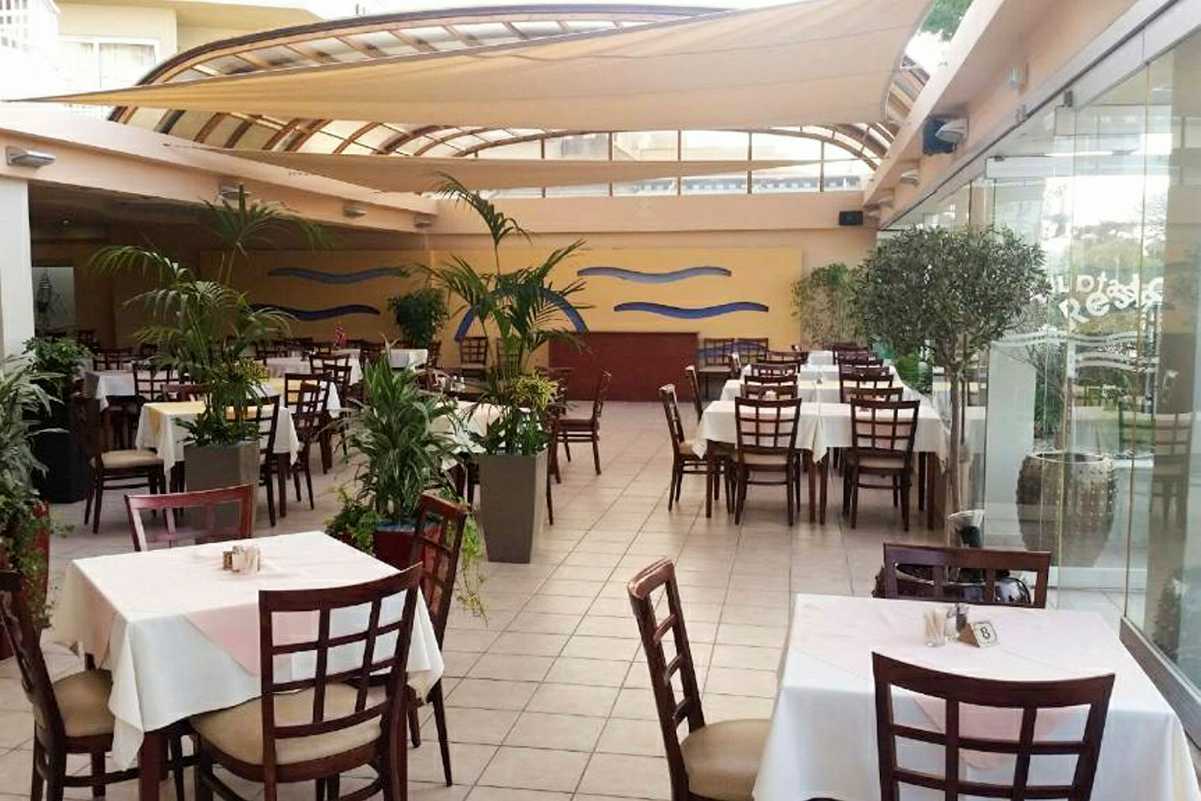 Bilde av en restaurant med bord og stoler, omgitt av planter. (AI-generert tekst)