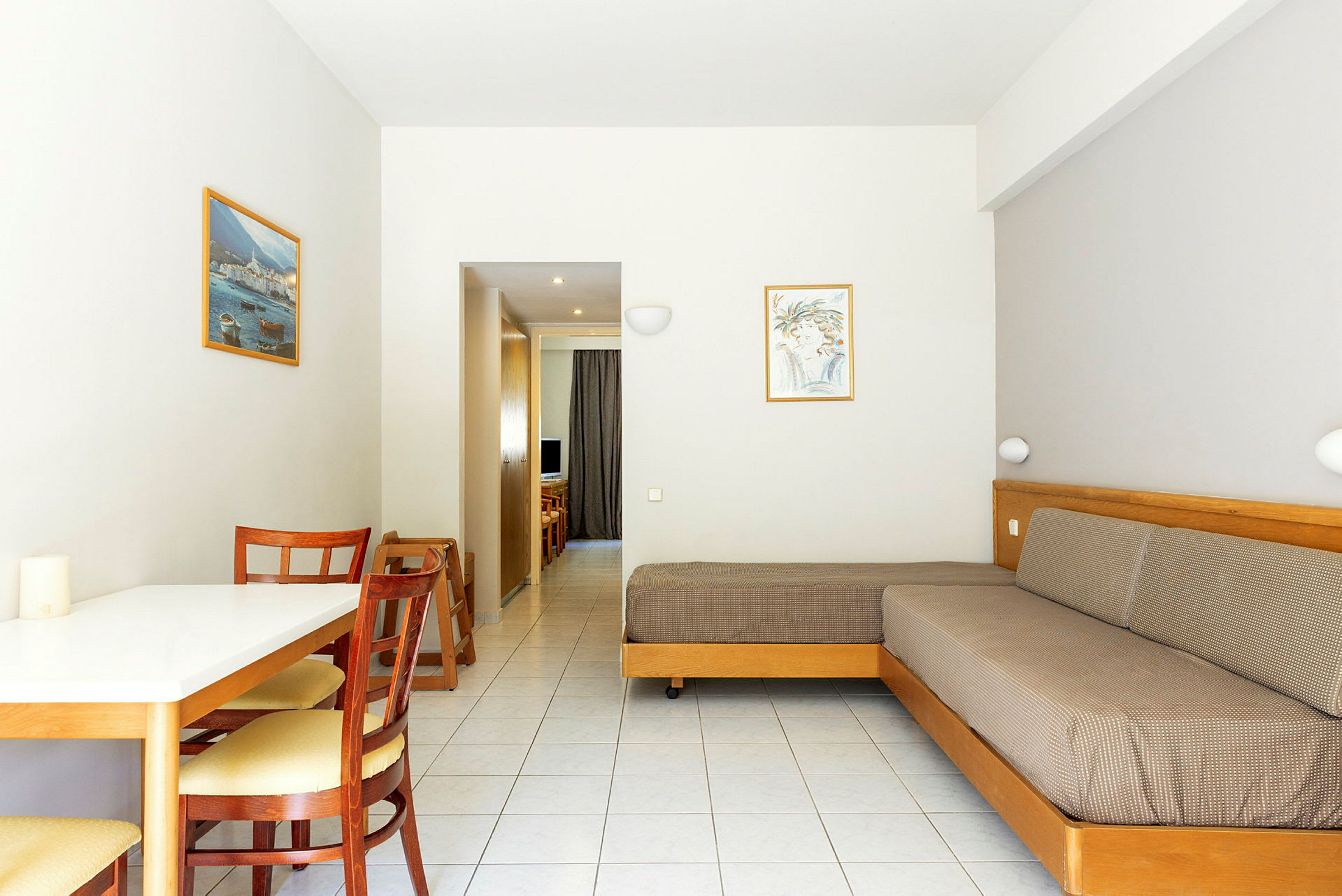 Bilde av et hotellrom med et bord, stoler, en sofa og utsikt mot en korridor. (AI-generert tekst)