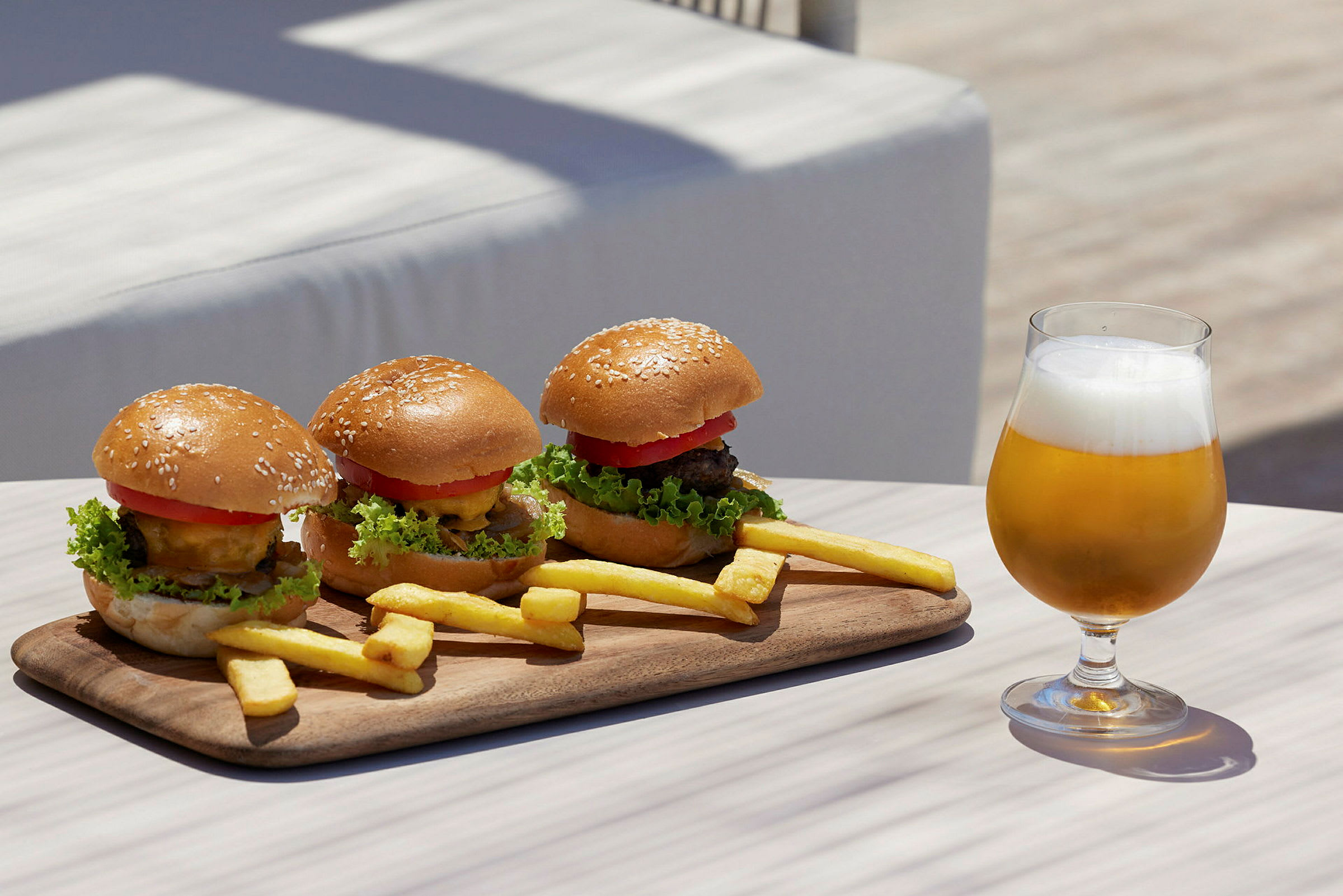 En trebrett med tre hamburgere og pommes frites samt et glass øl på et bord. (AI-generert tekst)