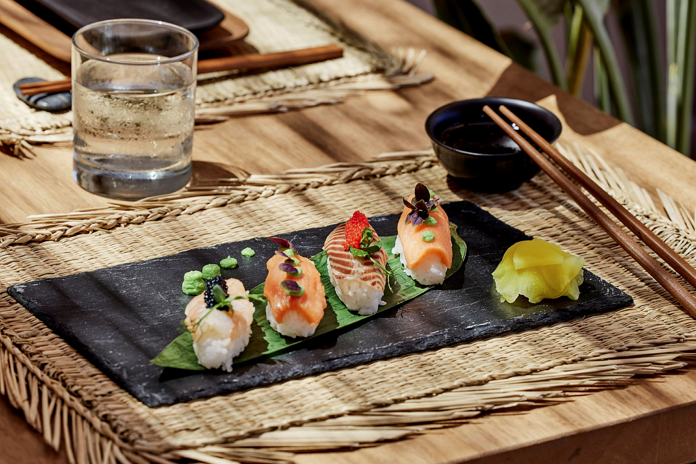 Sushibiter på et svart fat med en kanne vann og spisepinner ved siden av. (AI-generert tekst)