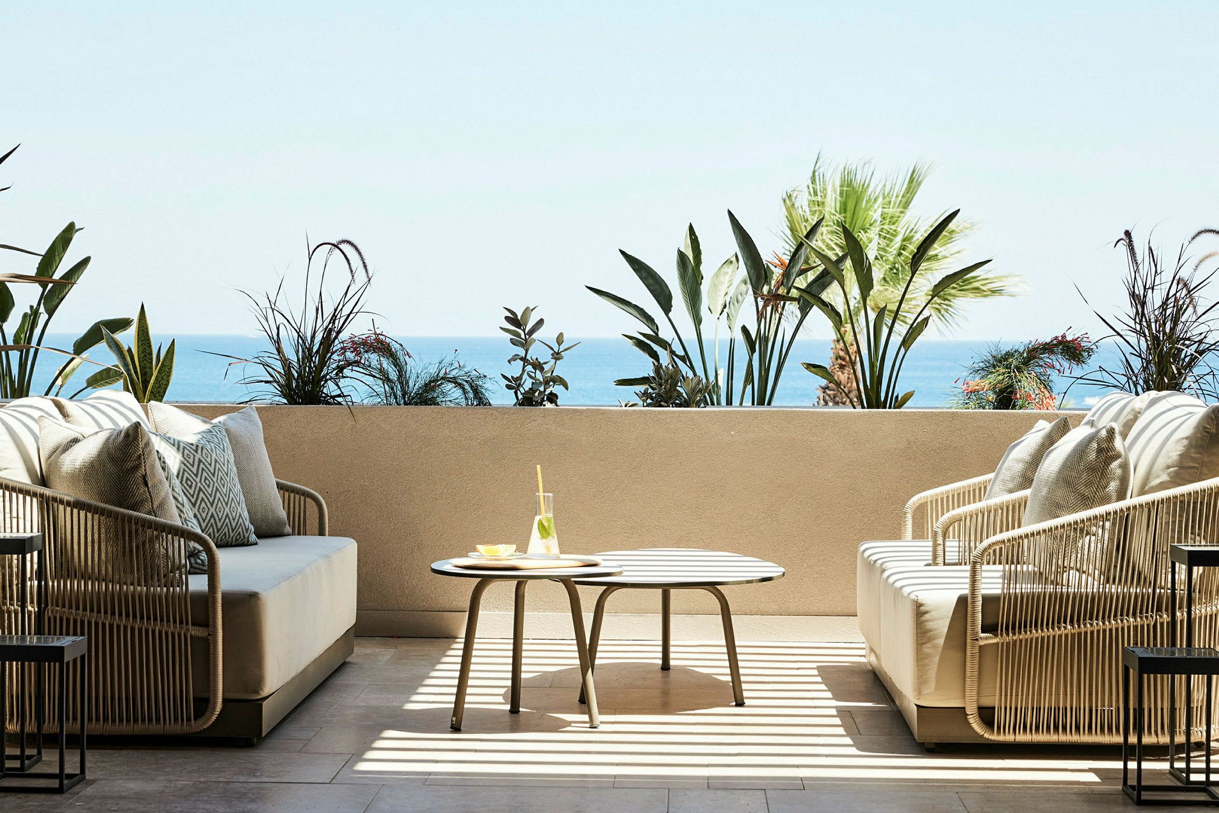 Terrasse med sittemøbler, bord med glass og hav i bakgrunnen. (AI-generert tekst)