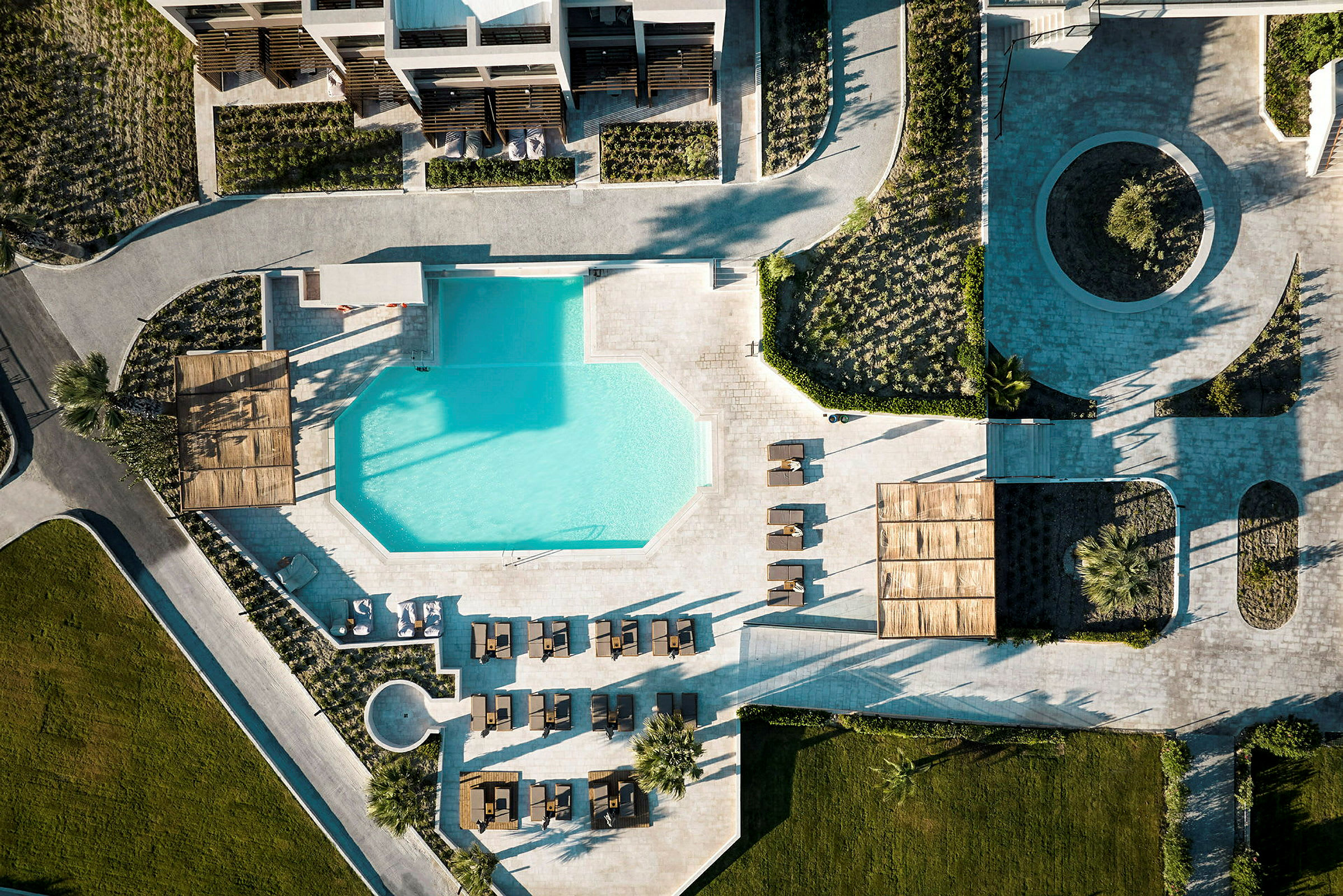 Flyfoto av en resort med geometrisk formet basseng omgitt av solsenger og grøntområder. (AI-generert tekst)