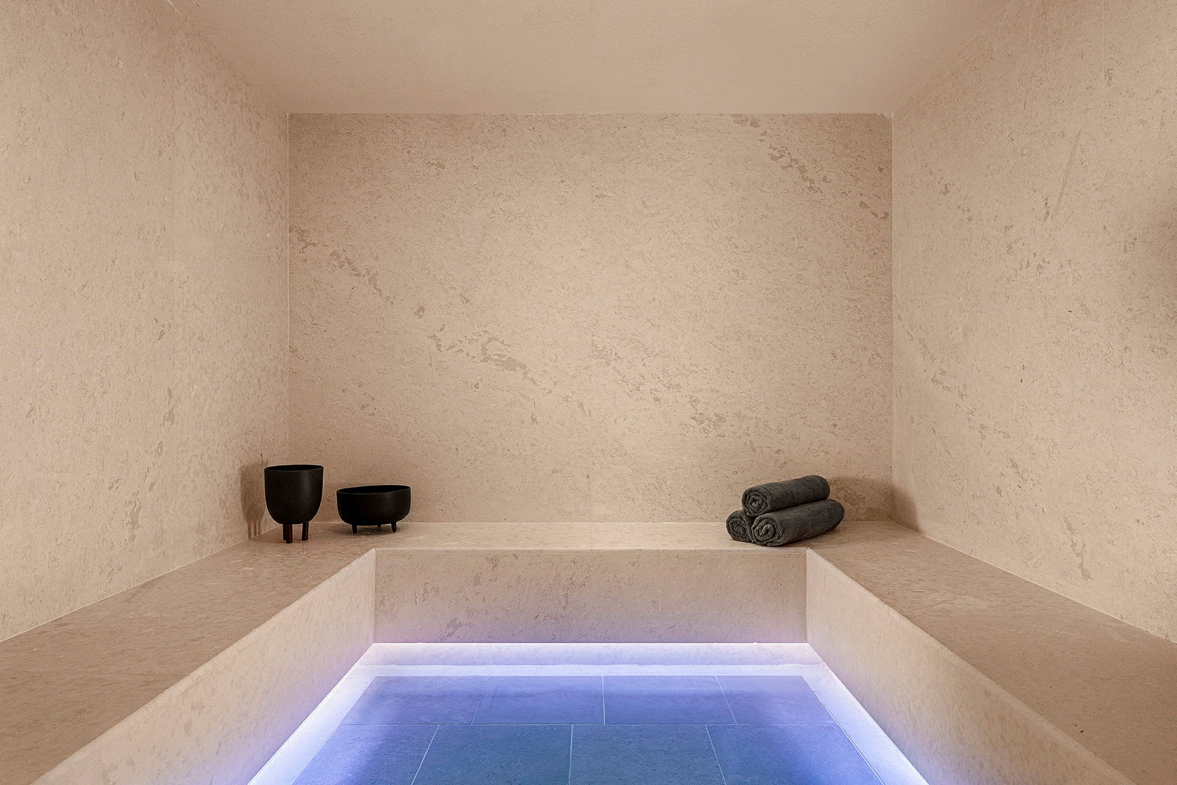 Et moderne spa-rom med minimalistisk innredning, benkesete, grå rullede håndklær og to mørke dekorative skåler. (AI-generert tekst)