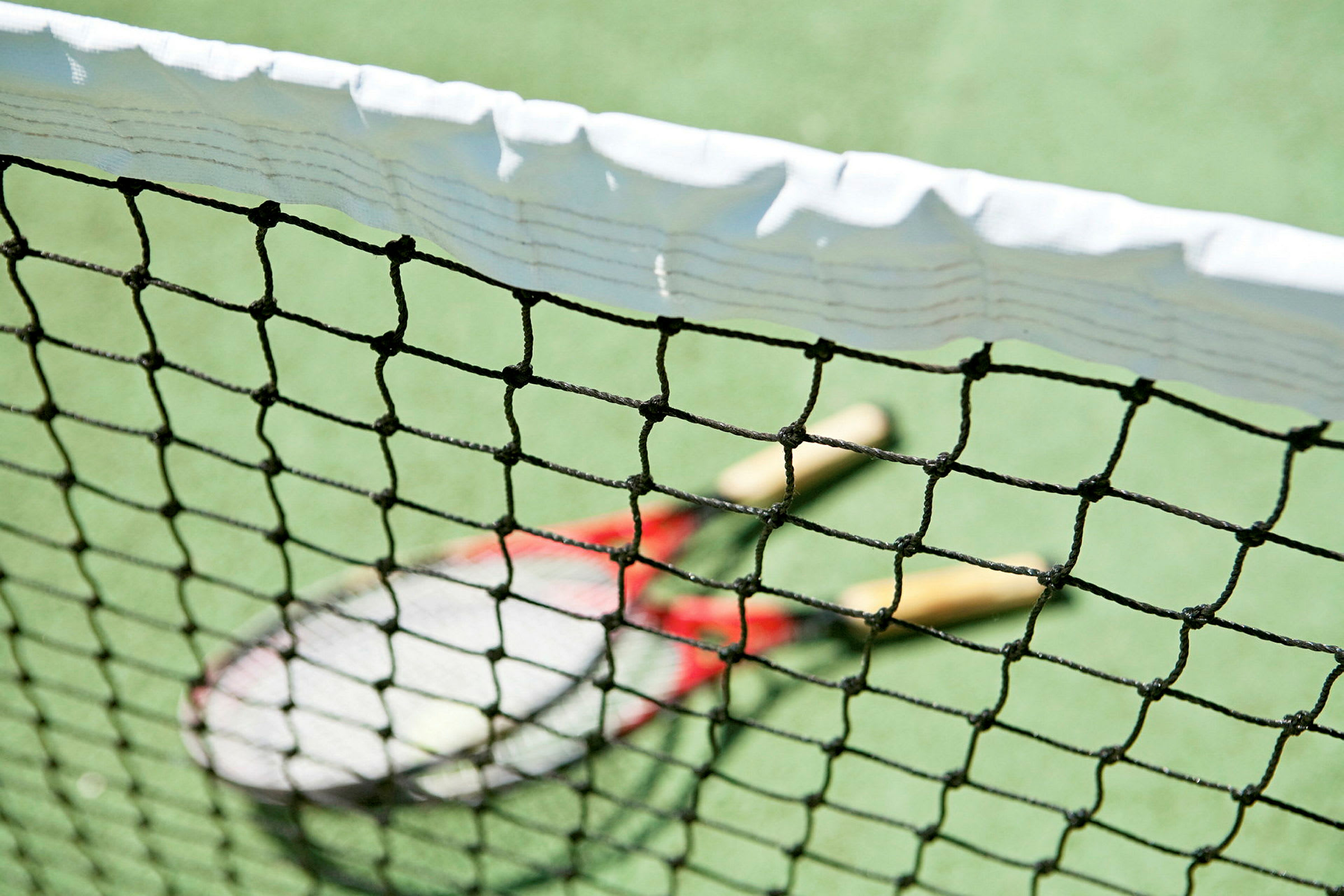 Nærbilde av et tennisnett med to tennisracketer på banen bak. (AI-generert tekst)