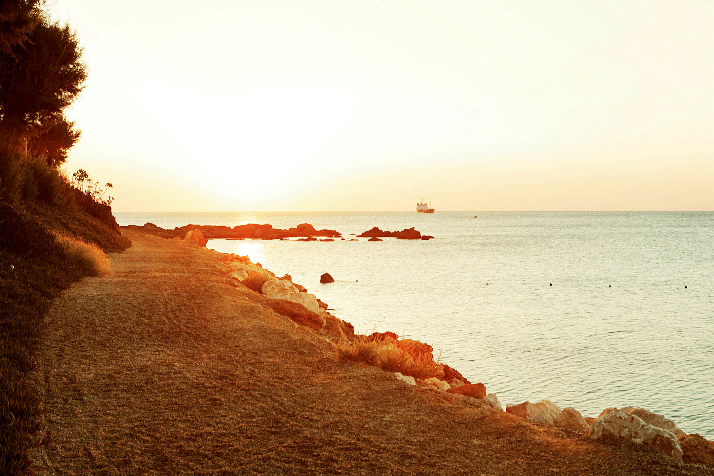 Strandpromenade i solnedgang med hav og et skip i det fjerne. (AI-generert tekst)