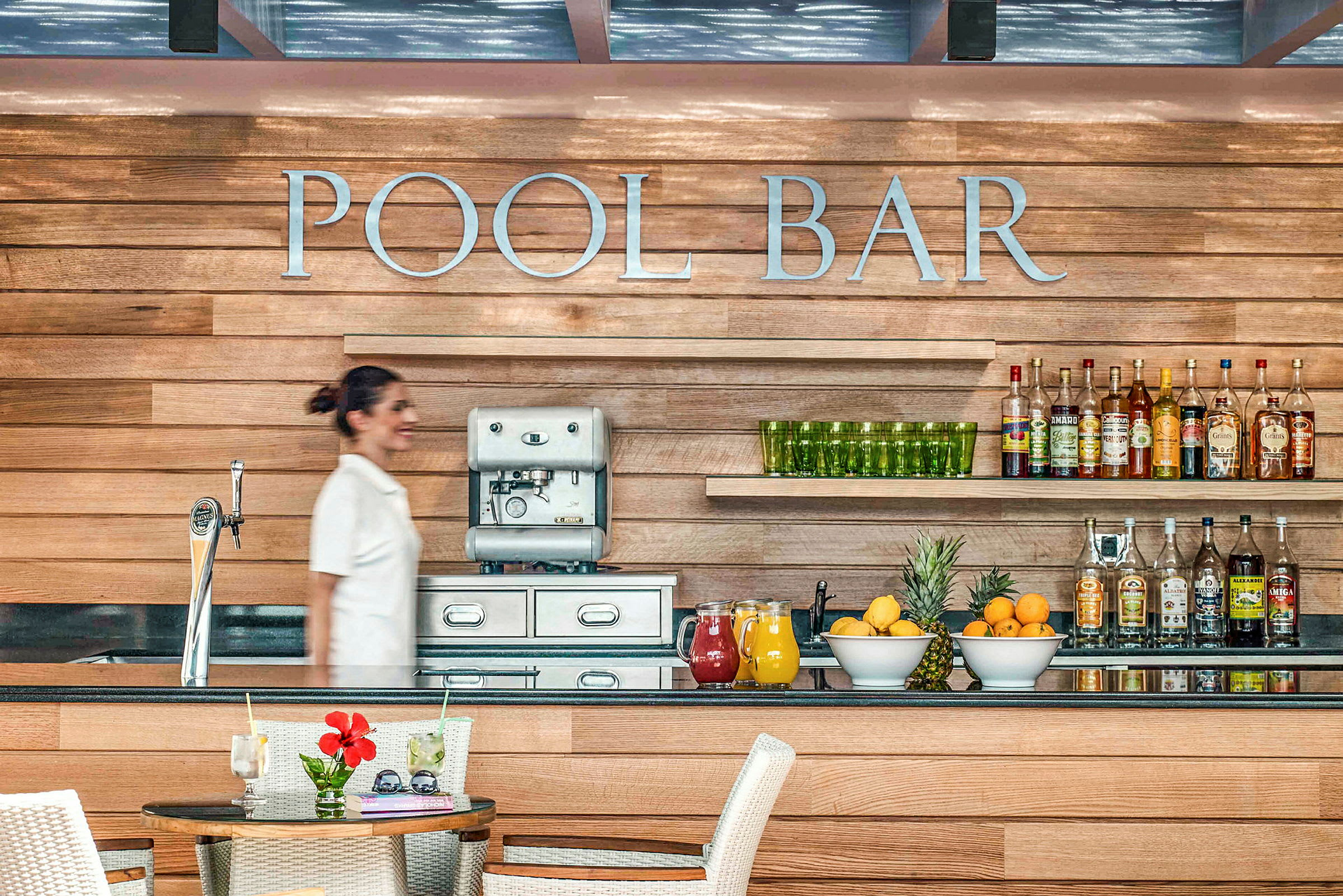 Bilde av en bassengbar med trepaneler, en kaffemaskin, drikkevarer og fersk frukt på benken. (AI-generert tekst)