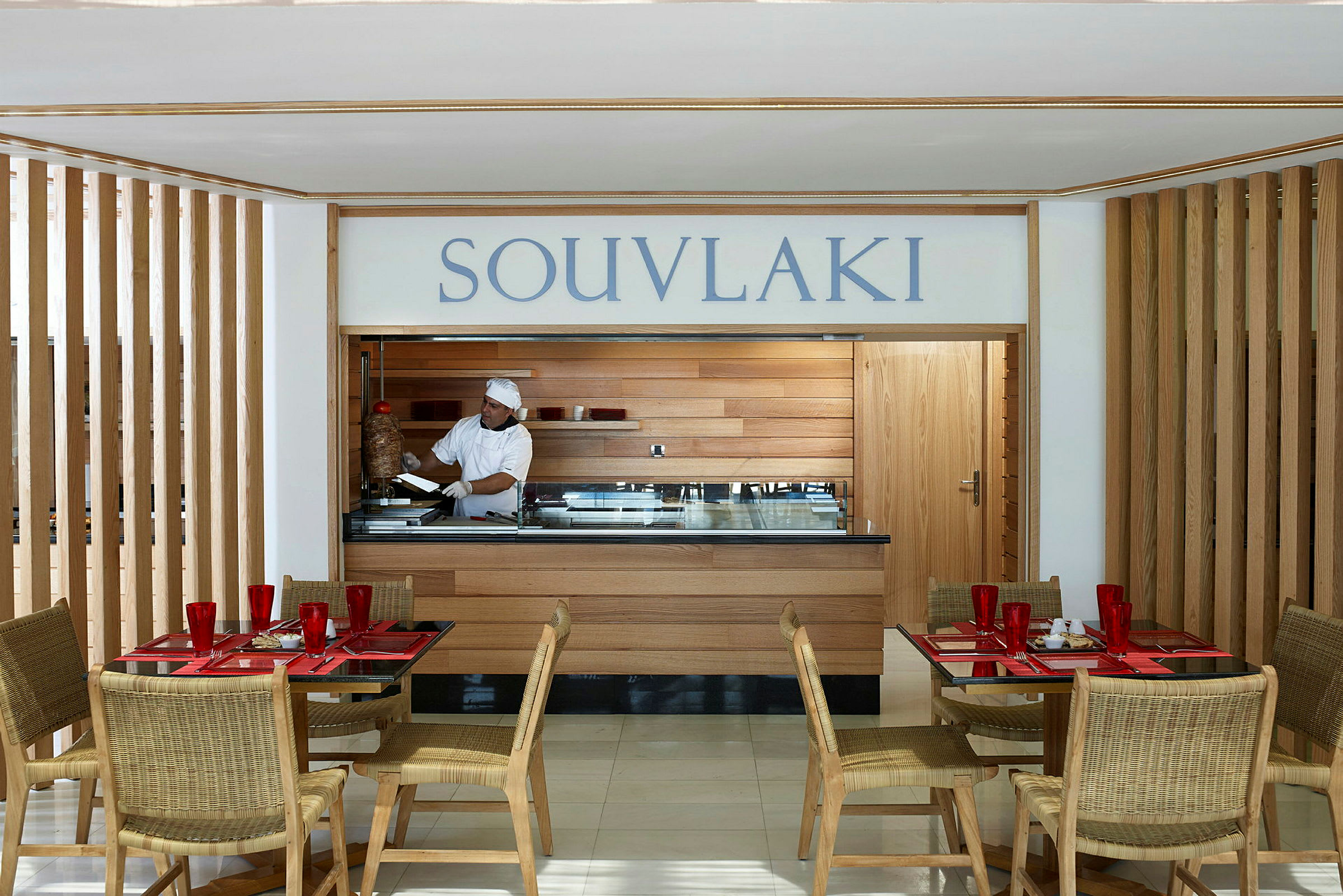 En restaurant med souvlaki-servering. Bord og stoler er plassert i forgrunnen. (AI-generert tekst)