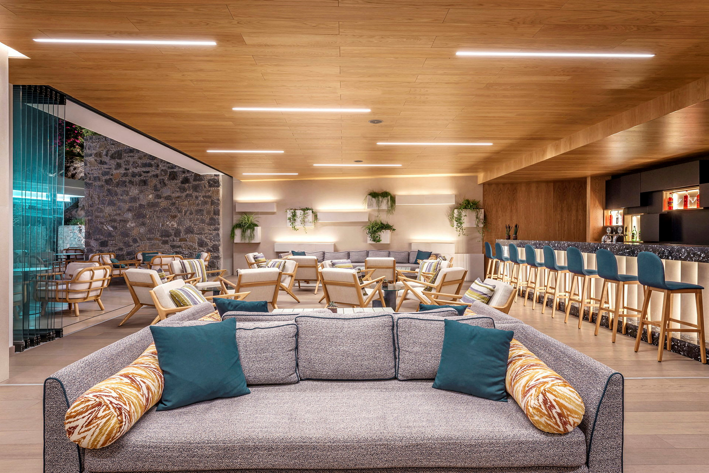 Et moderne og innbydende loungeområde med sofaer, lenestoler og en bar med sitteplasser. Innredningen er lys og luftig med trematerialer og grønt. (AI-generert tekst)