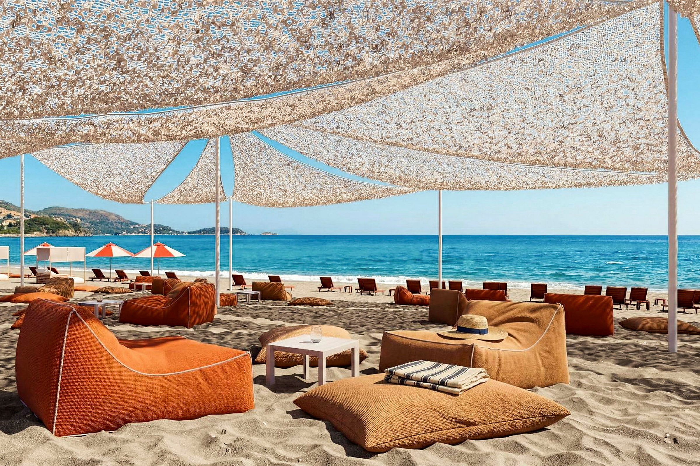 Strand med oransje sitteplasser under en solskjerming. Hav og blå himmel i bakgrunnen. (AI-generert tekst)