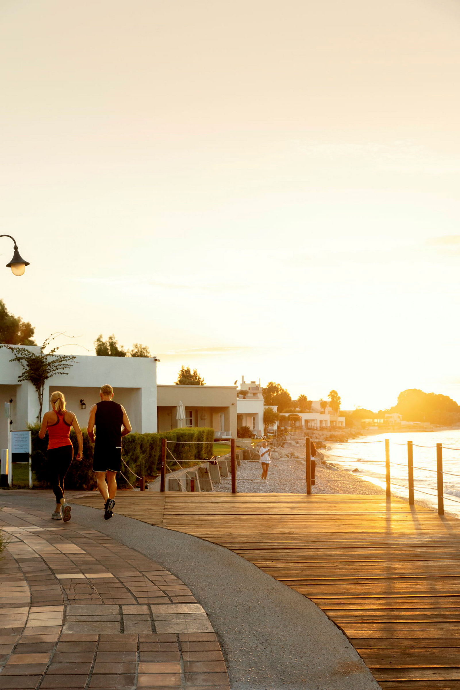 To personer jogger på en strandpromenade i solnedgangen. (AI-generert tekst)