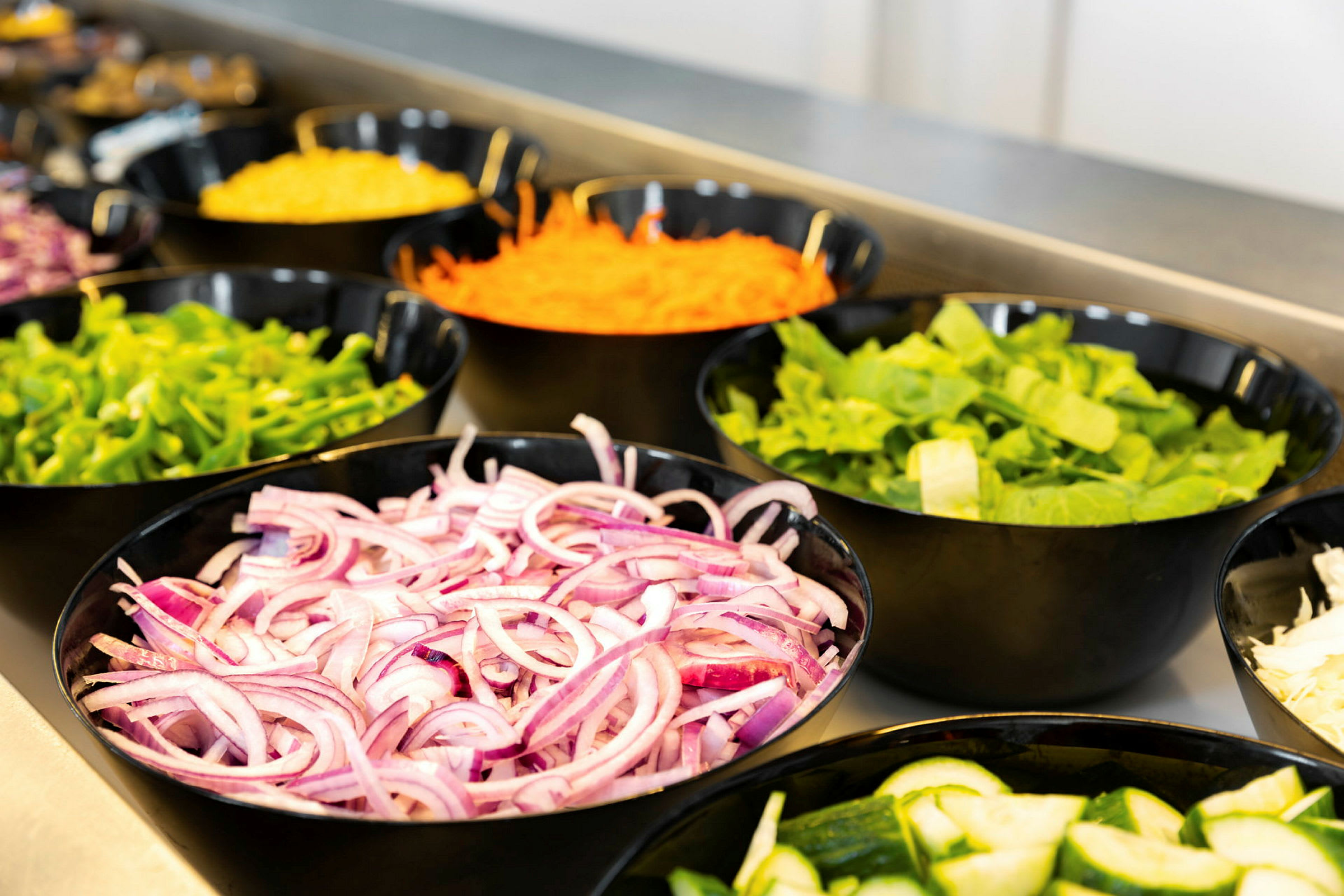 Skåler med forskjellige grønnsaker, inkludert rødløk, agurk, salat, paprika og revet gulrot. (AI-generert tekst)