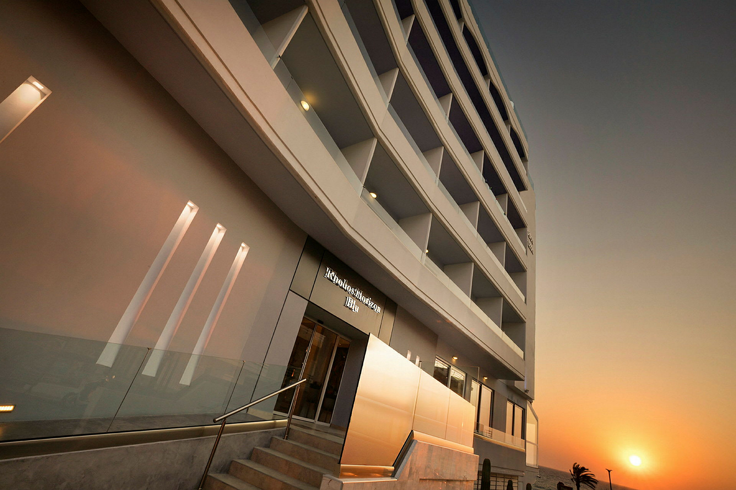 Moderne hotellbygning med flere etasjer mot en solnedgang. (AI-generert tekst)