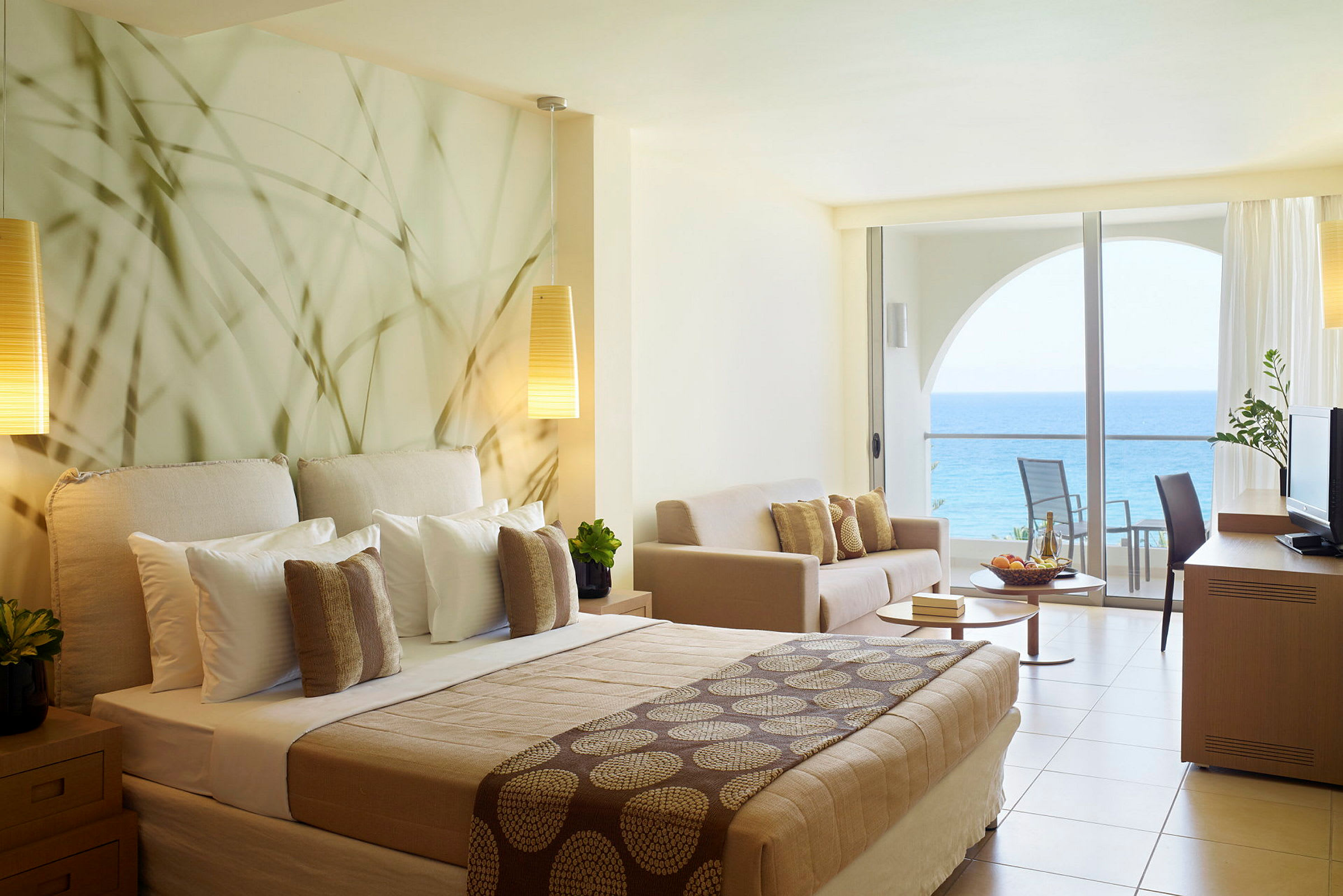 Hotellrom med havutsikt og moderne innredning inkludert seng, sofa og balkong. (AI-generert tekst)