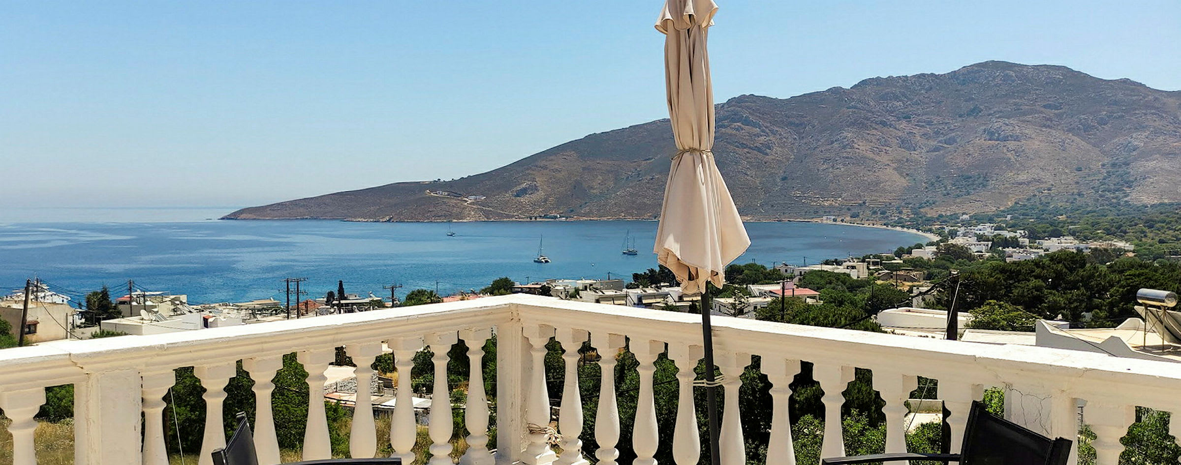 En utsikt fra en terrasse med rekkverk, en parasoll og havet og fjell i bakgrunnen. (AI-generert tekst)
