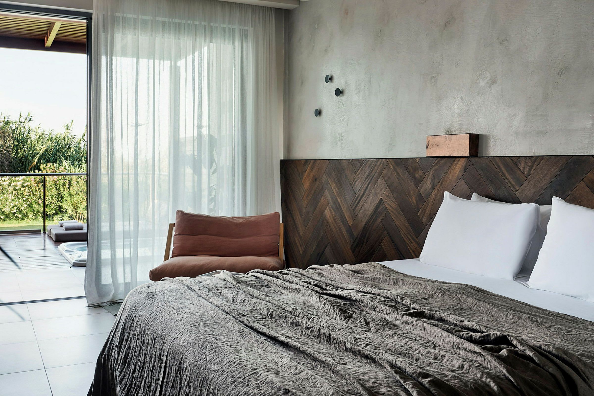 Et hotellrom med en stor seng, tremøbler og en stol ved siden av, samt glassdører som fører ut til en terrasse med utsikt over grøntområder. (AI-generert tekst)