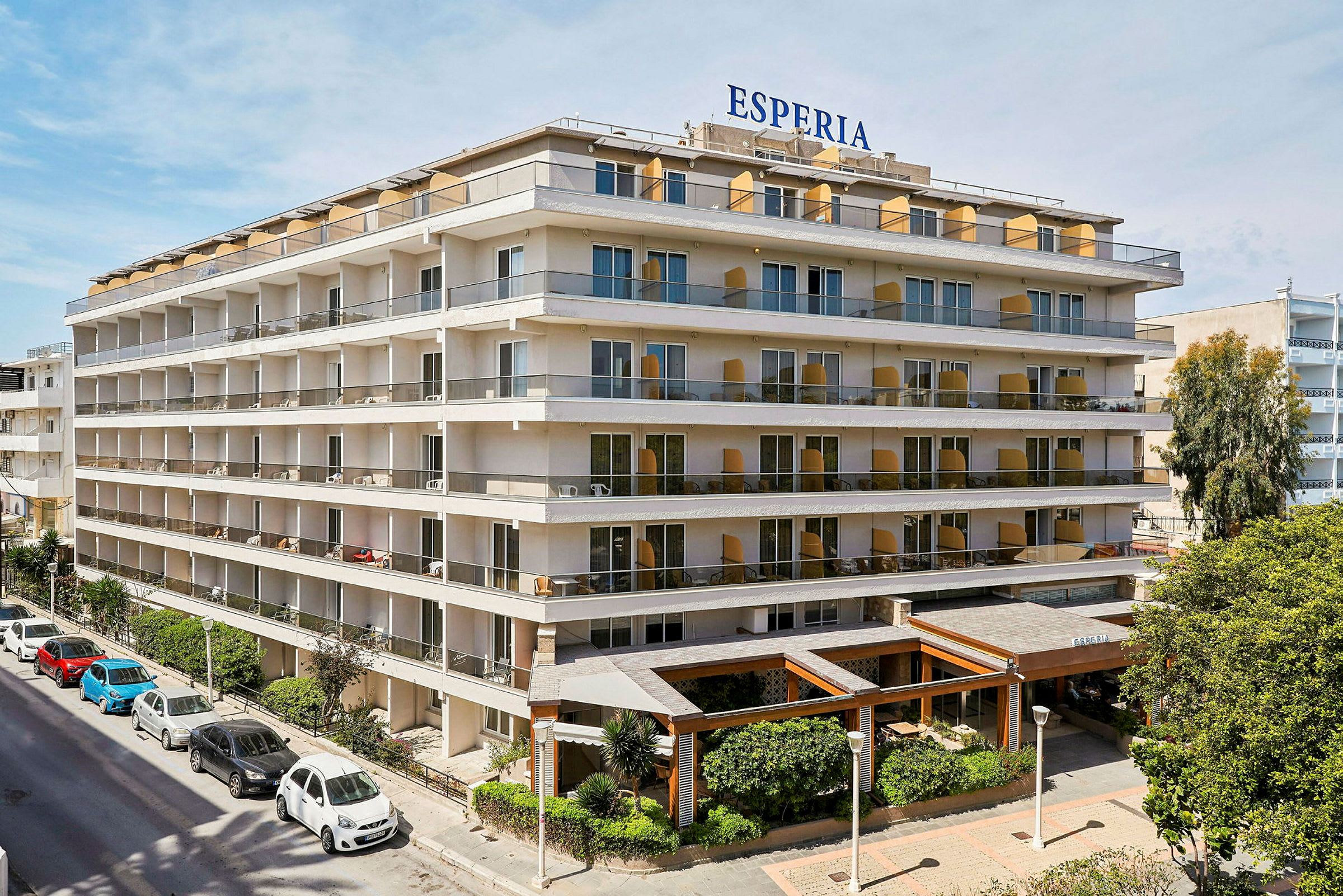 Hotel Esperia, en fleretasjes bygning med store balkonger og grønne beplantninger ved inngangen. (AI-generert tekst)