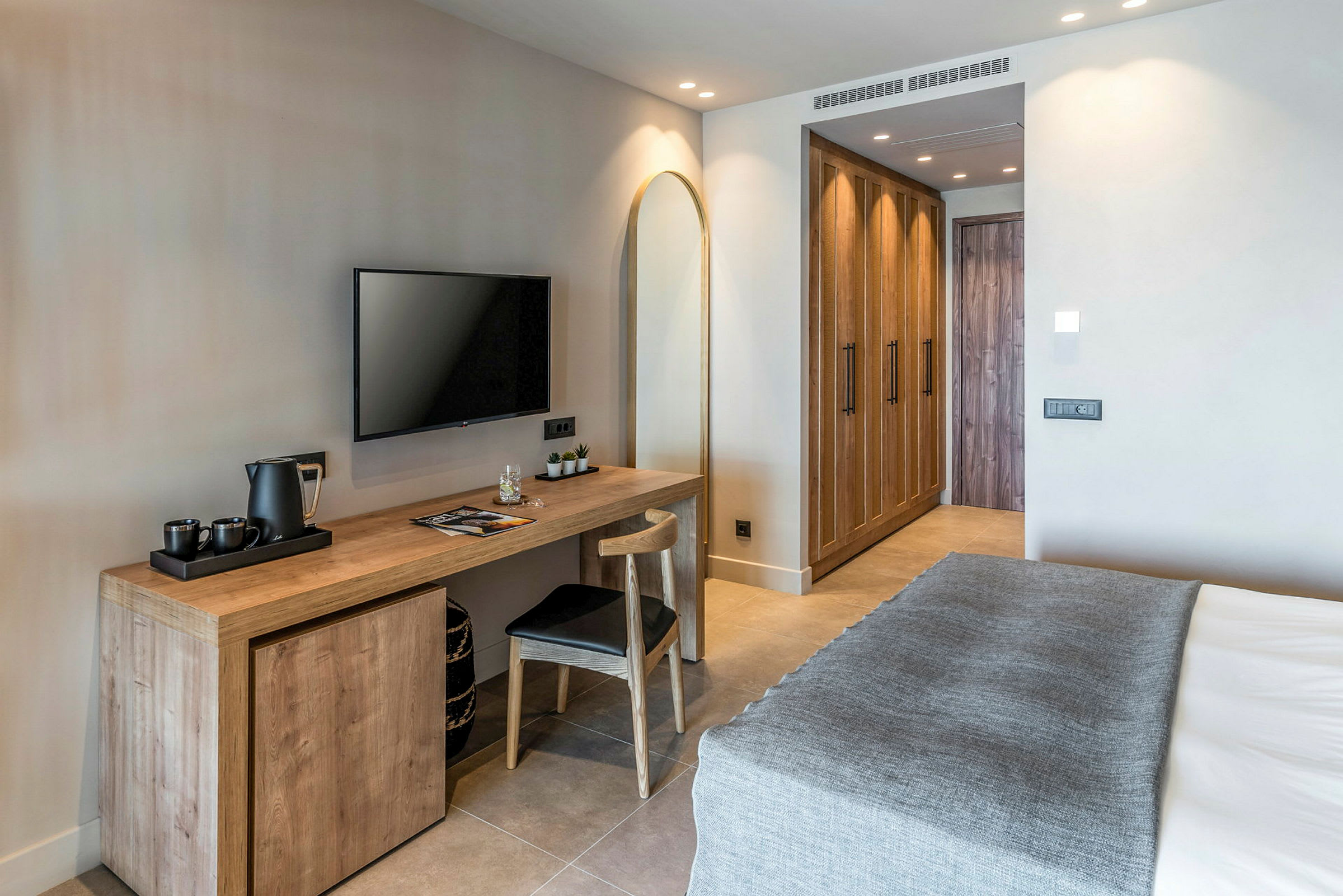 Et moderne hotellrom med en seng, skrivebord, stol, veggmontert TV og garderober. (AI-generert tekst)