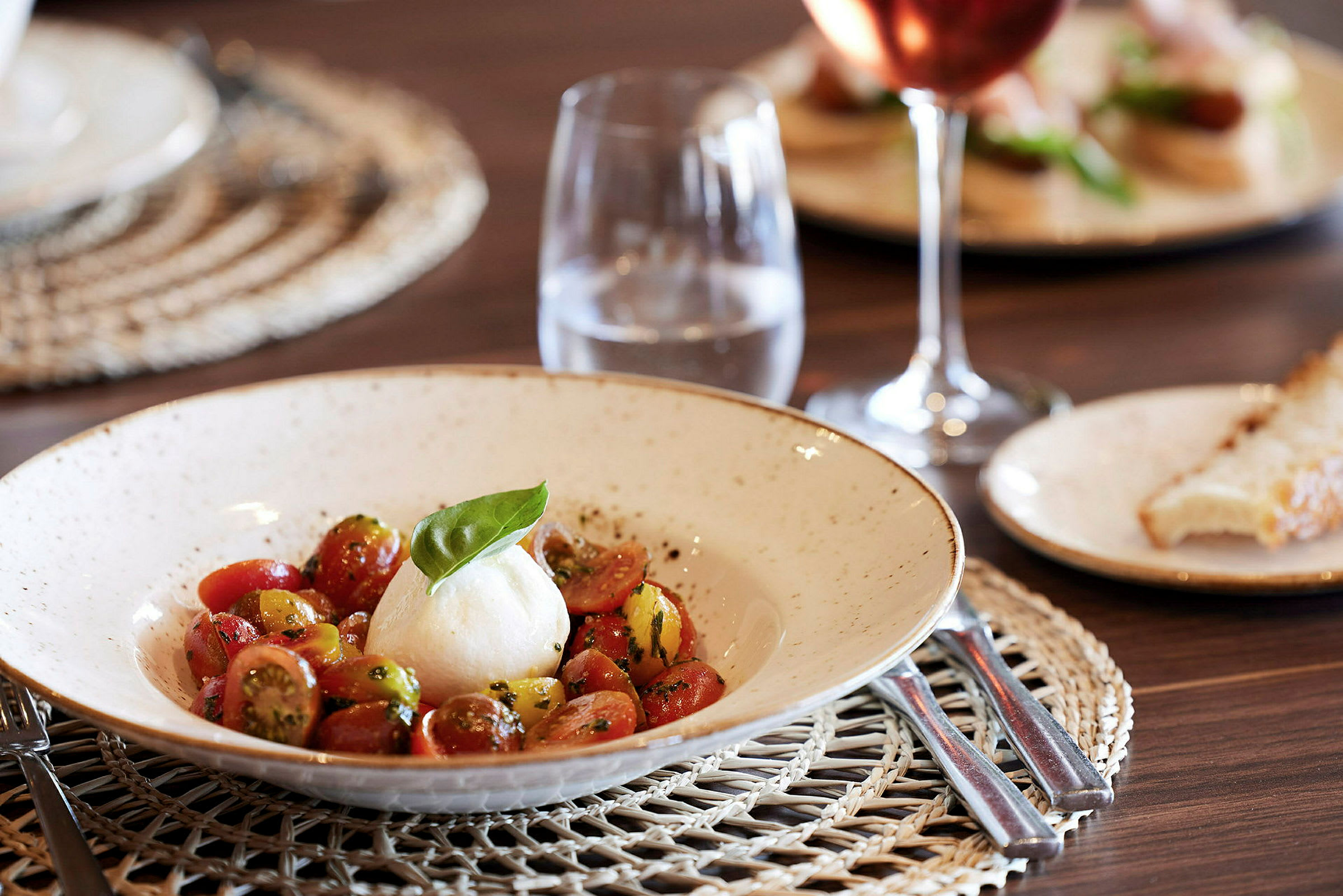 En tallerken med mozzarella og tomatsalat, samt et glass vann på et bord. (AI-generert tekst)