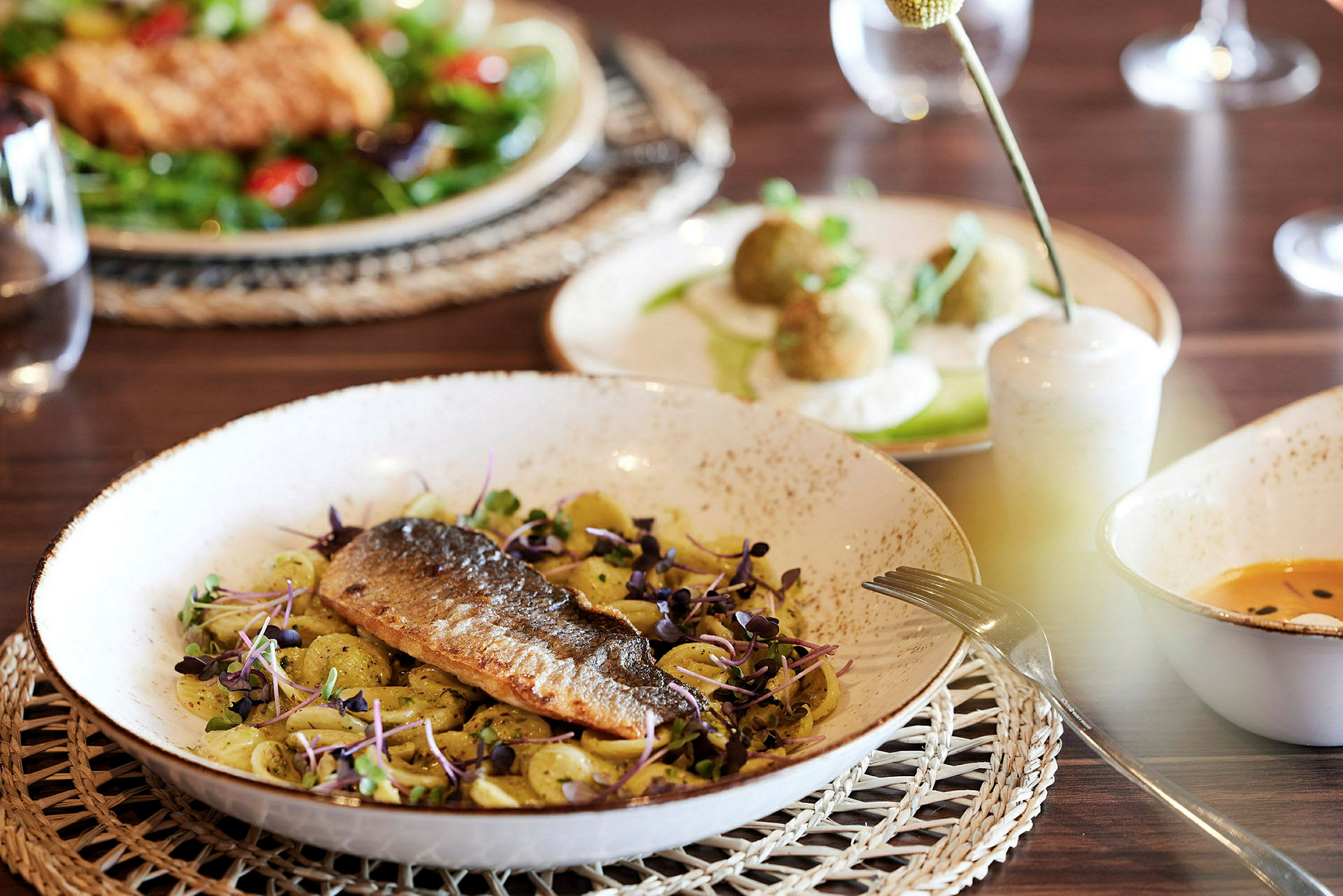 En tallerken med fisk og pasta, omgitt av andre retter på et bord. (AI-generert tekst)