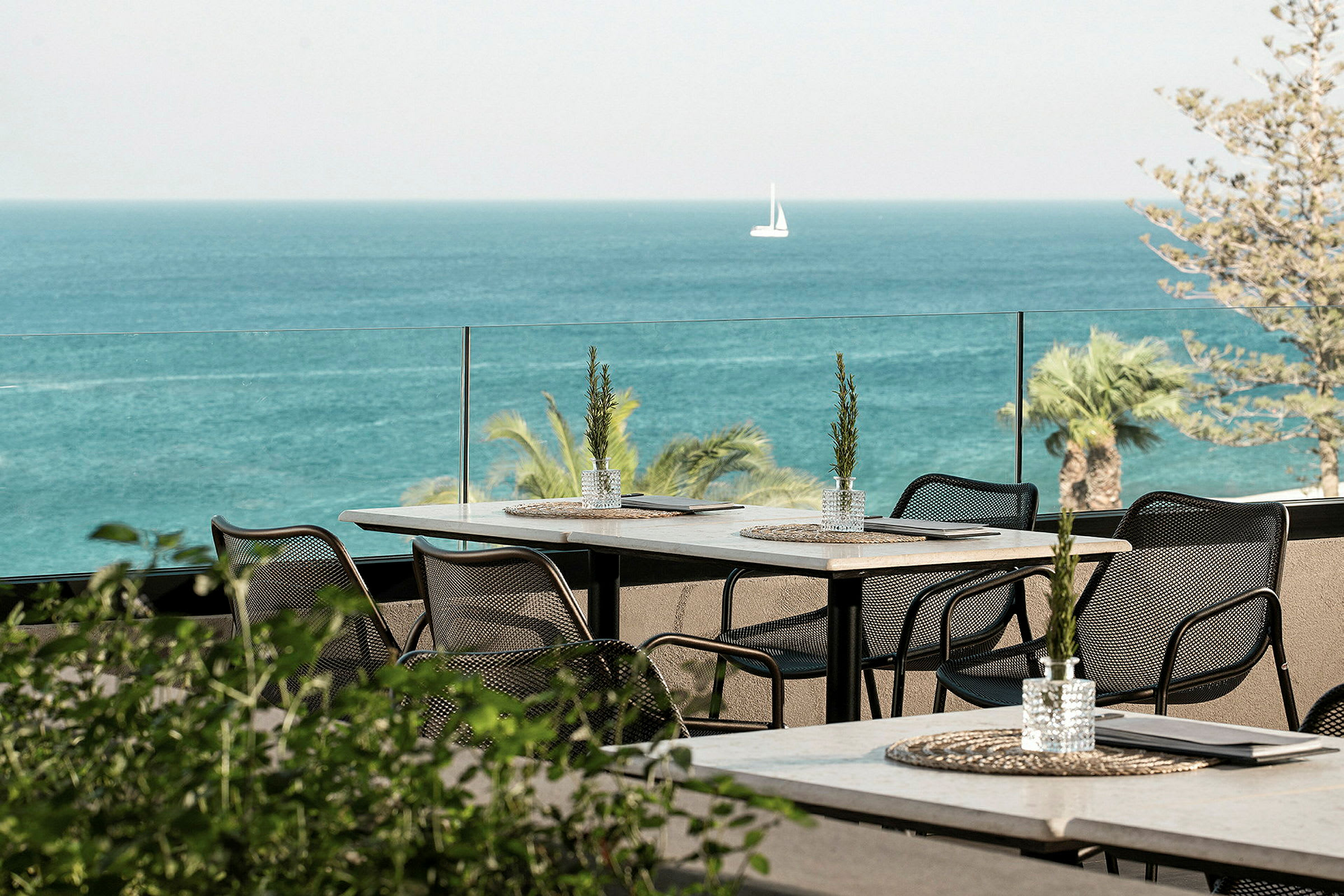 Utsikt fra en terrasse med bord og stoler mot havet. (AI-generert tekst)