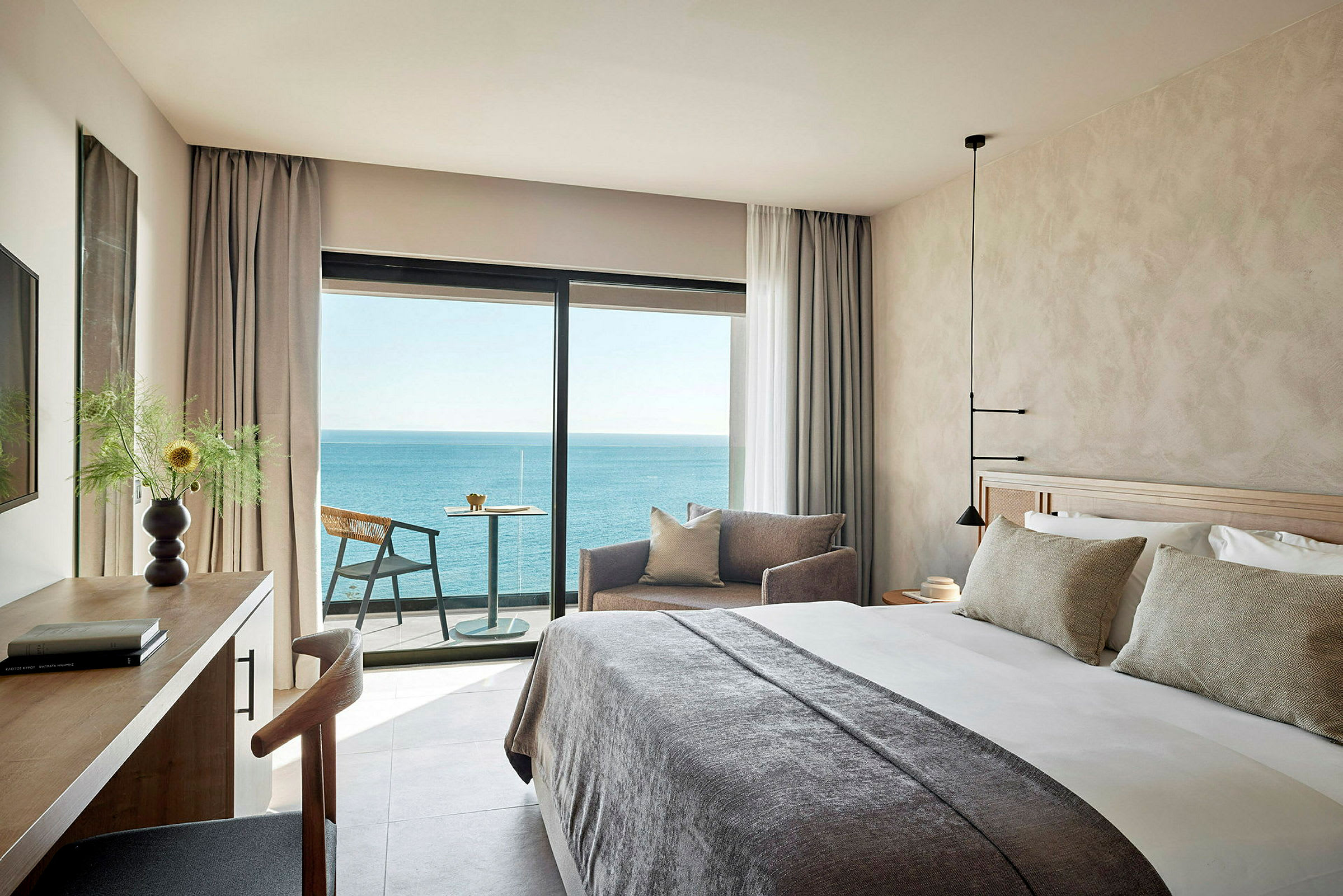 Et moderne hotellrom med en stor seng, sofadel og skrivebord, samt en balkong med utsikt over havet. (AI-generert tekst)