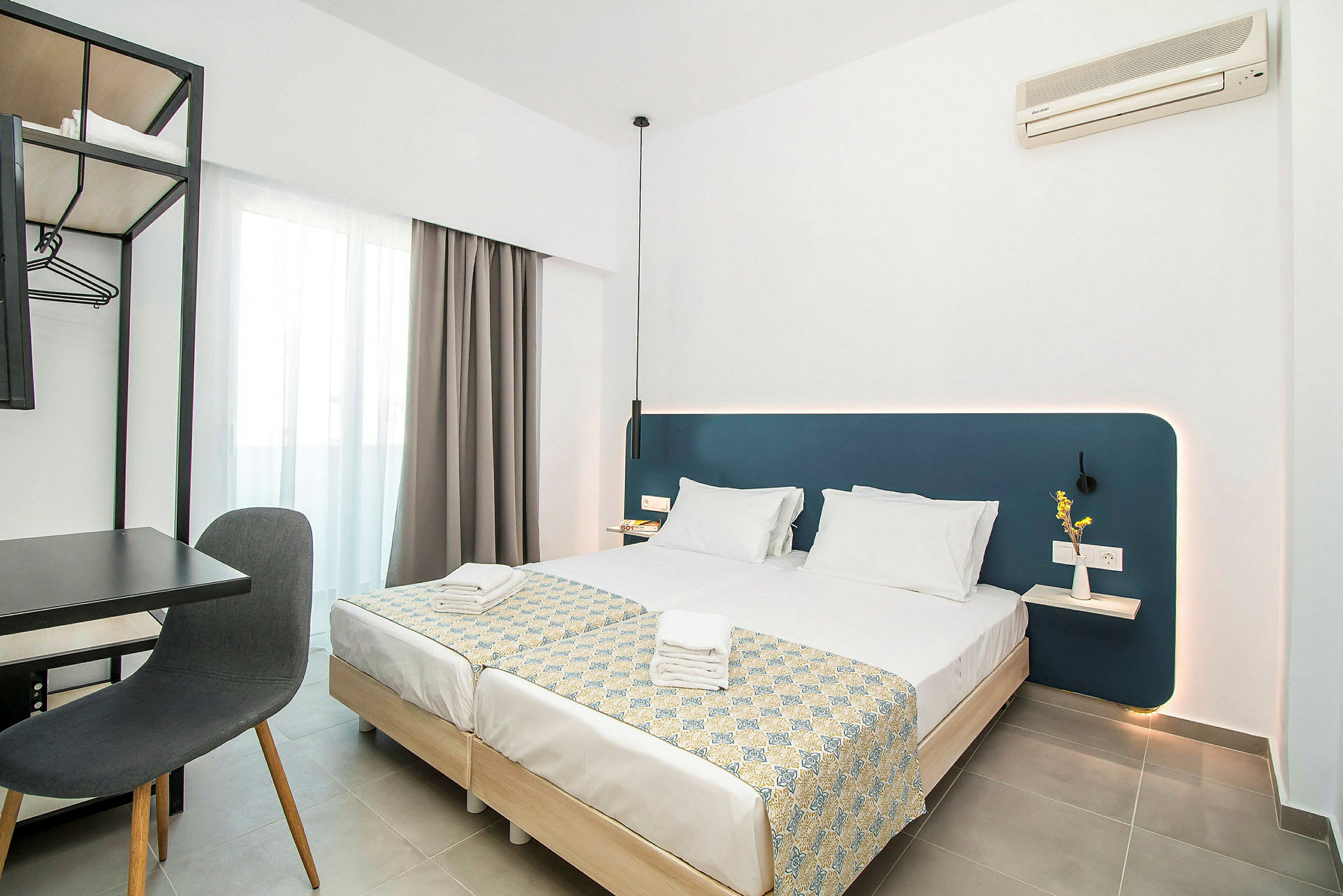 Moderne hotellrom med to oppredde enkeltsenger, skrivebord og stol samt veggmontert klimaanlegg. (AI-generert tekst)