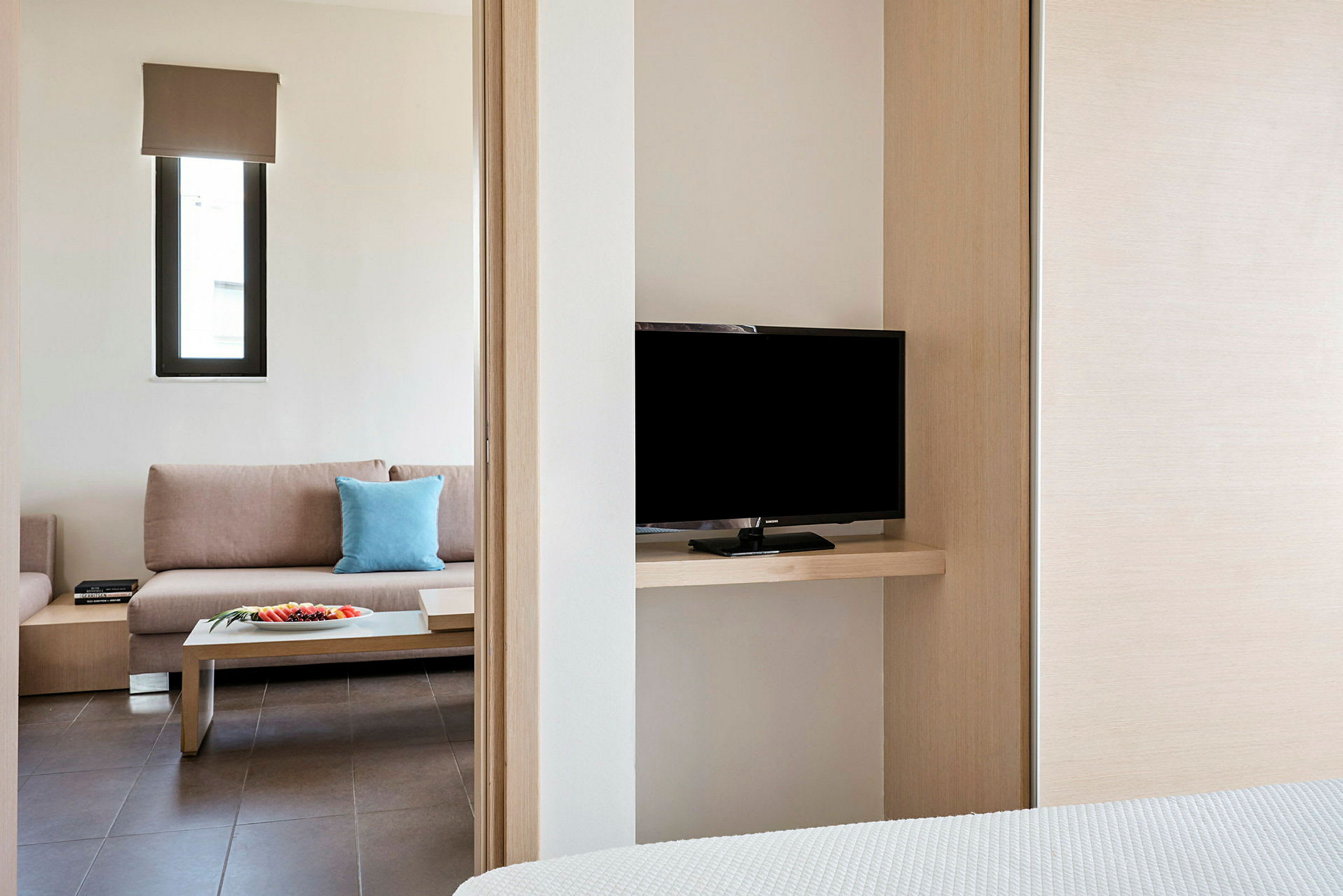 Et hotellrom med en sofa, et sidebord og en TV synlig fra soverommet. (AI-generert tekst)