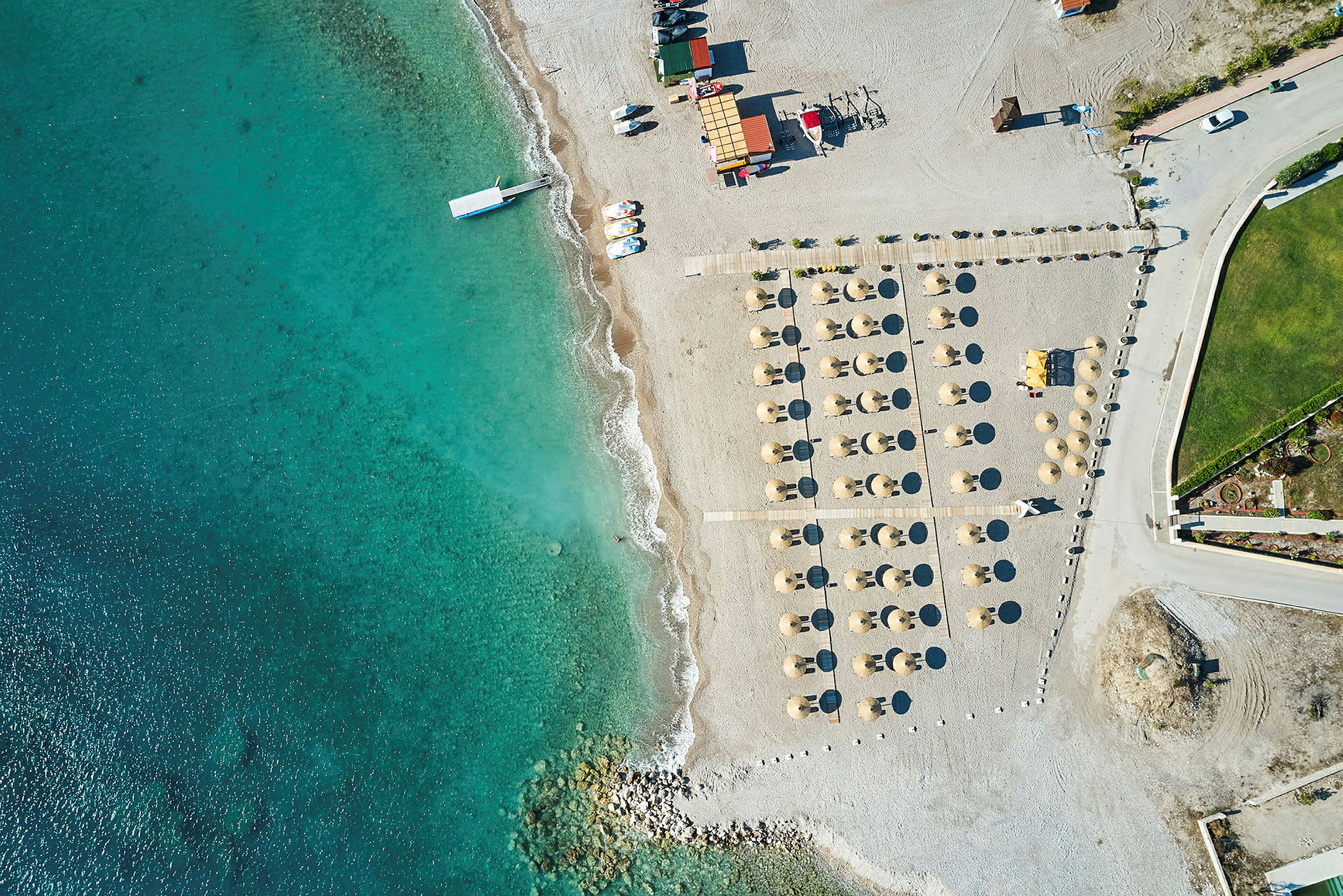 Luftfoto av en strand med parasoller og solsenger ved siden av klart blått vann. (AI-generert tekst)