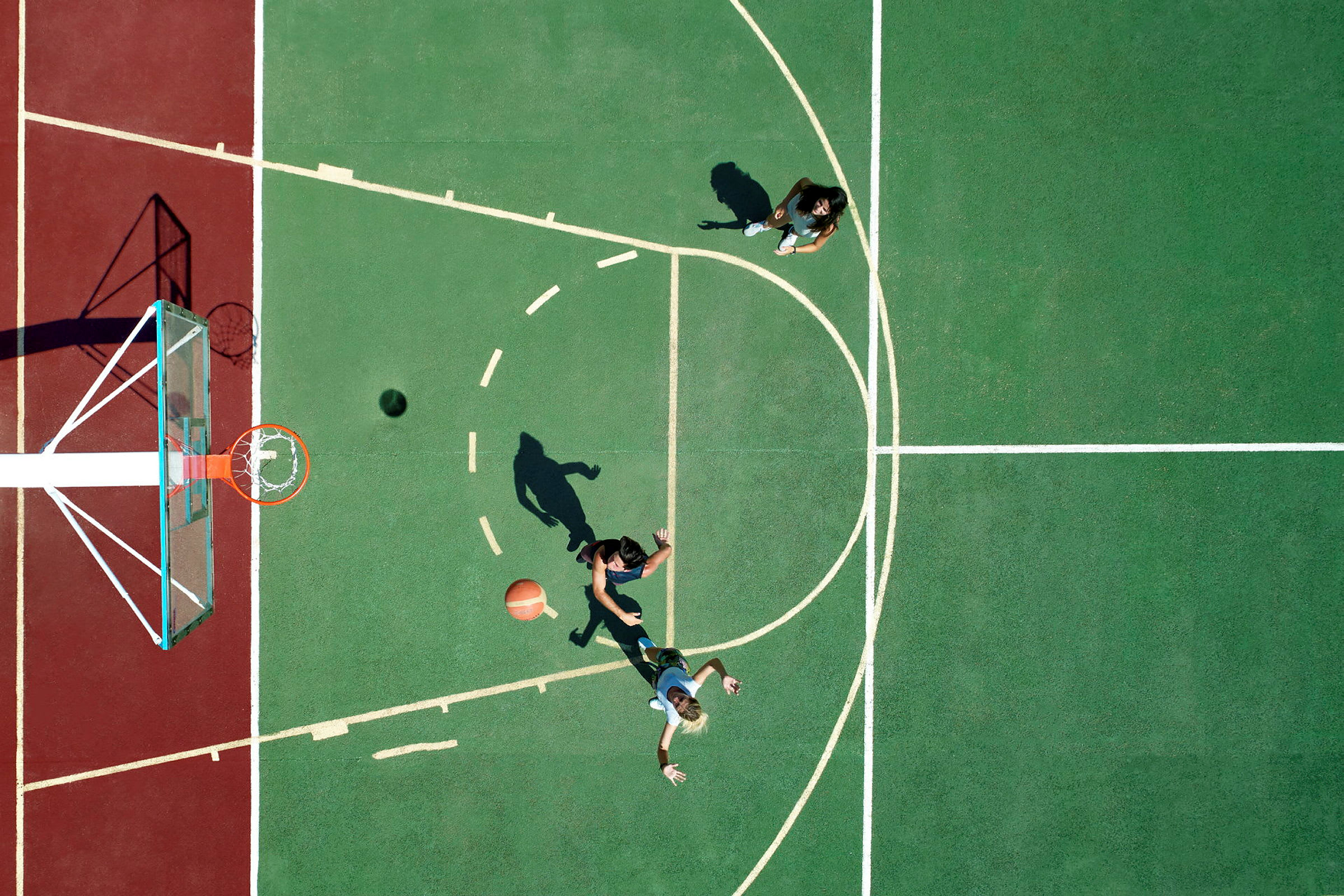 To personer spiller basketball på en utendørsbane, sett ovenfra. (AI-generert tekst)