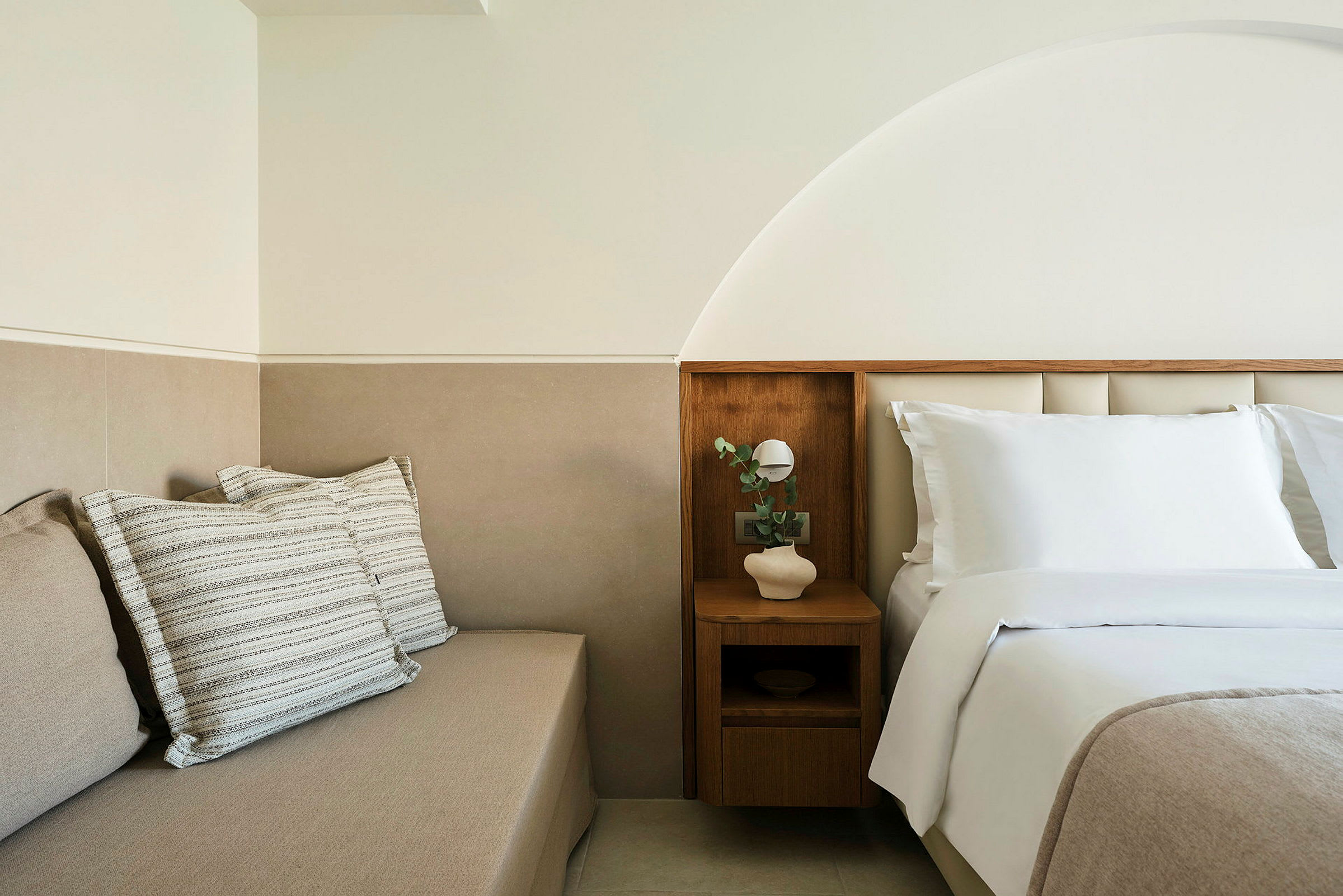 Et lyst og moderne hotellrom med en oppredd seng og en sittemøbel med puter. (AI-generert tekst)