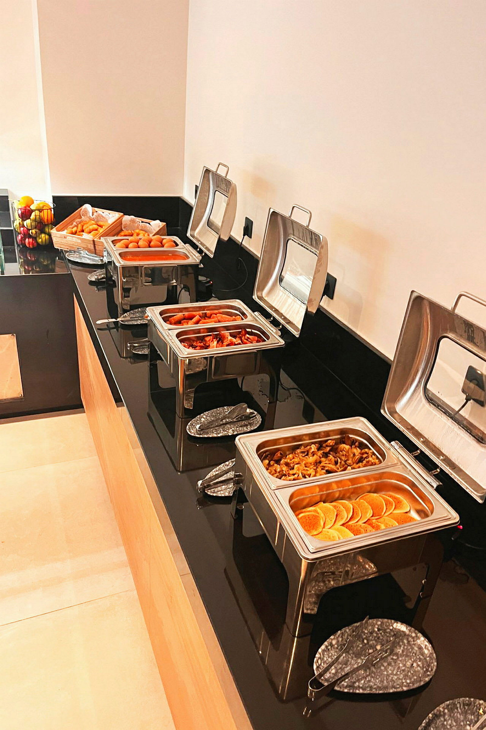 Buffetbord med varm mat i serveringsfat og frisk frukt ved siden av. (AI-generert tekst)