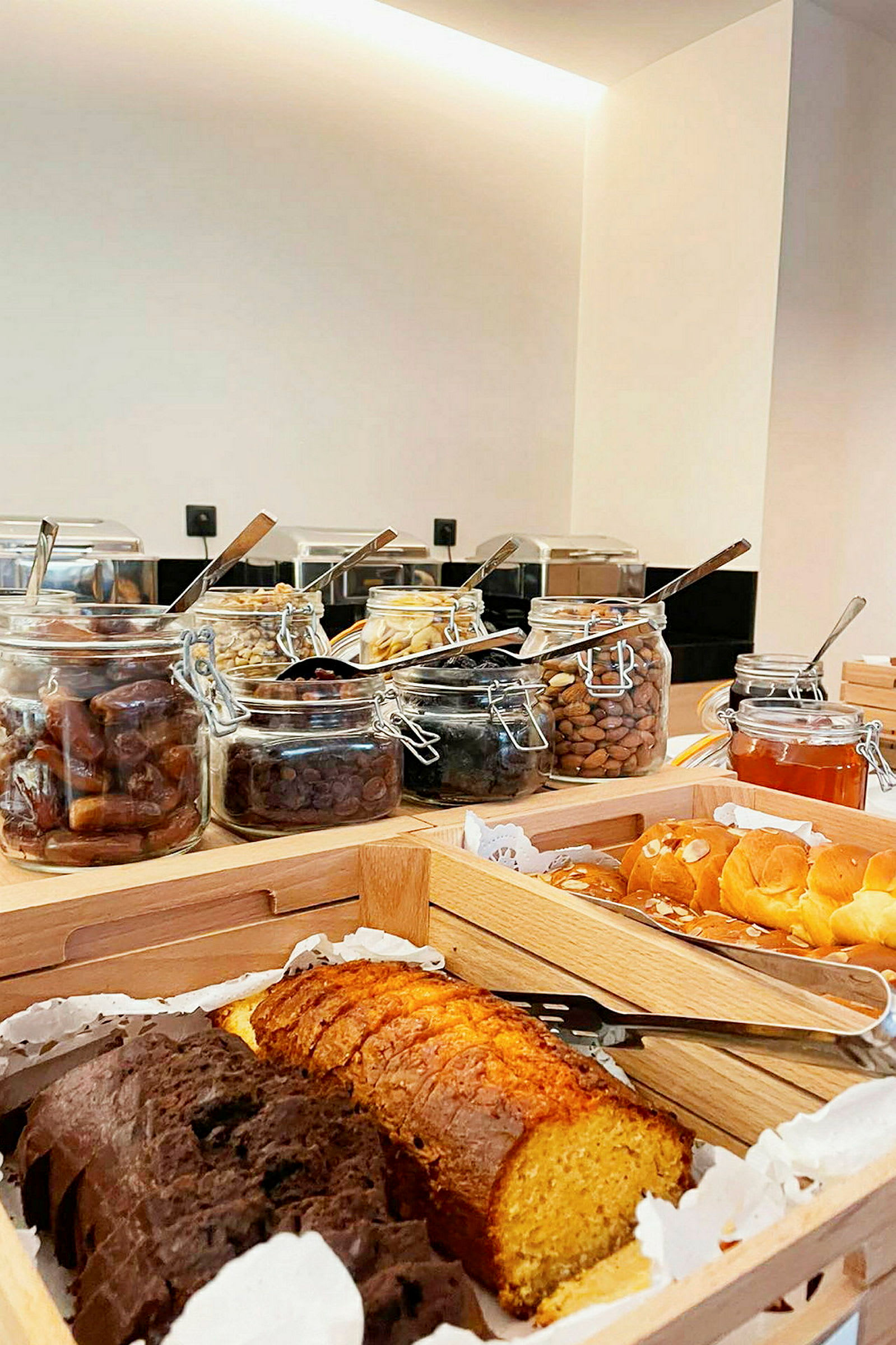 Bilde av en frokostbuffé med ulike brød, bakverk og krukker fylt med nøtter og tørket frukt. (AI-generert tekst)