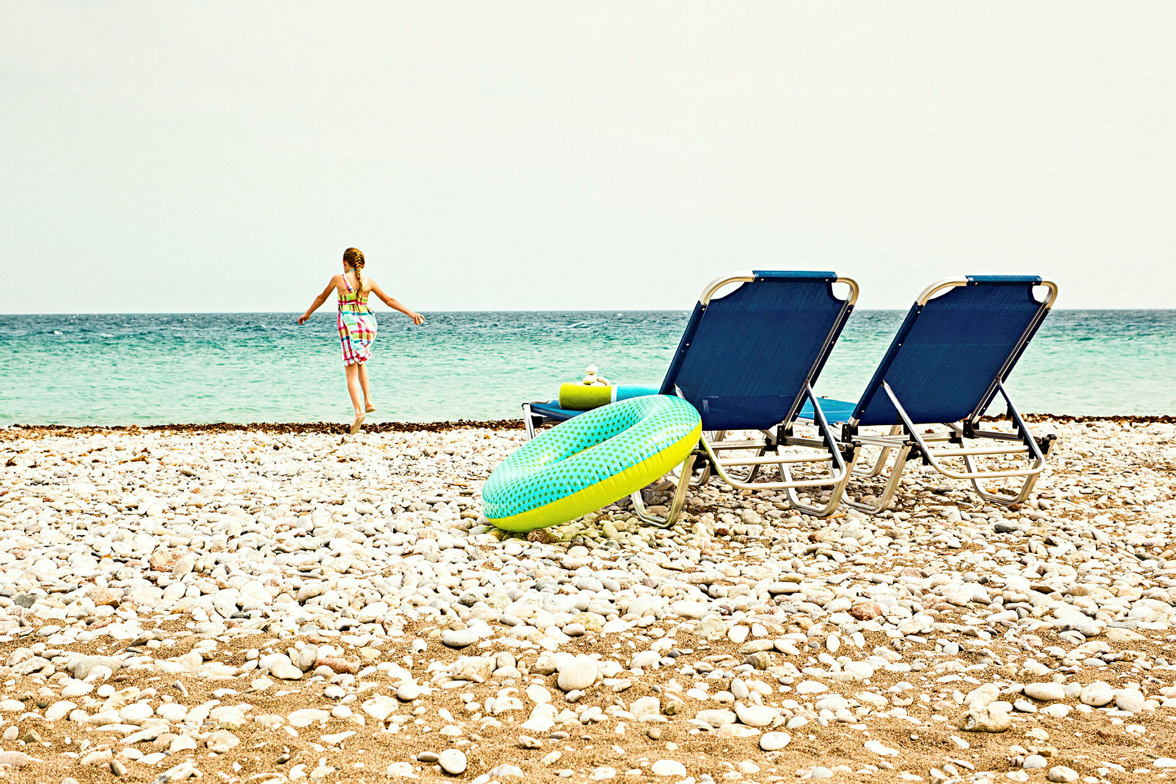 En strand med stoler, en badering og en person som går mot havet. (AI-generert tekst)