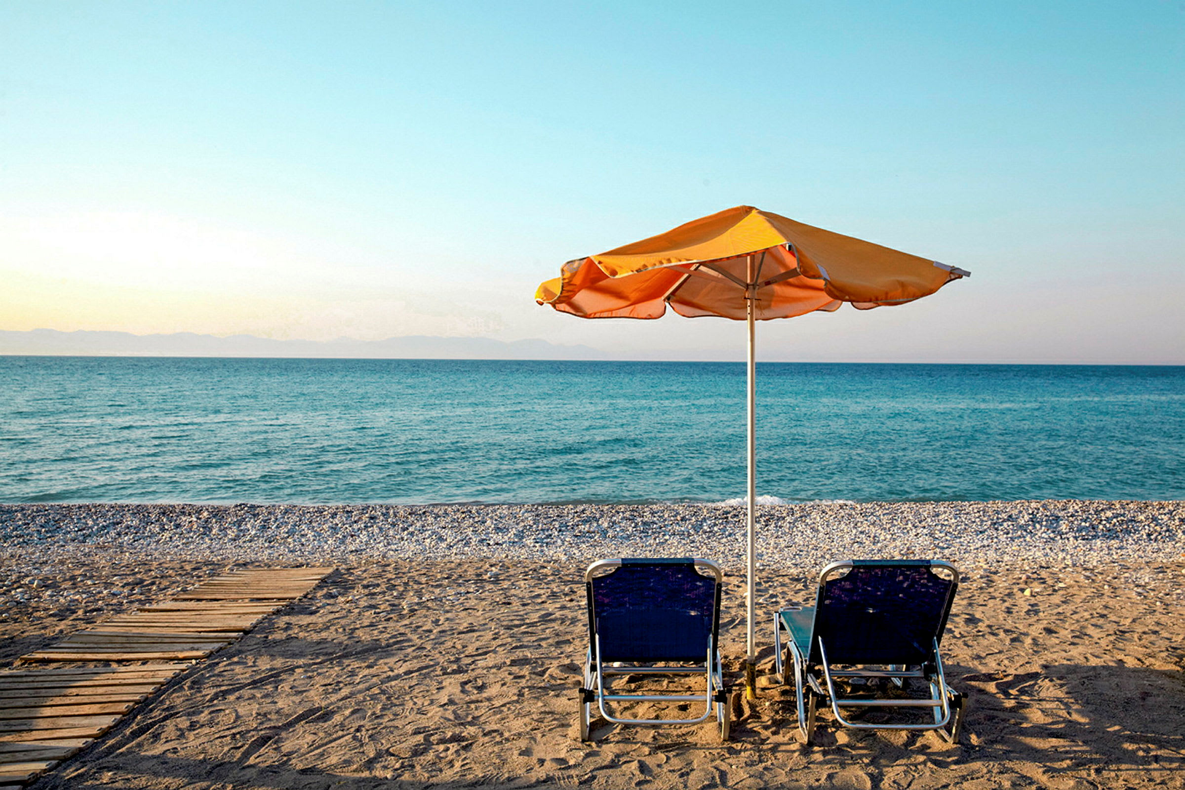 To solsenger og en parasoll på en strand med utsikt over havet. (AI-generert tekst)
