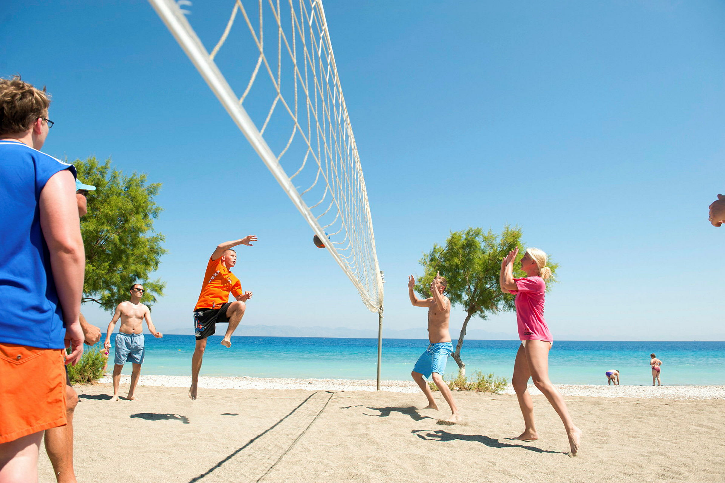 Personer spiller volleyball på en sandstrand nær sjøen. (AI-generert tekst)