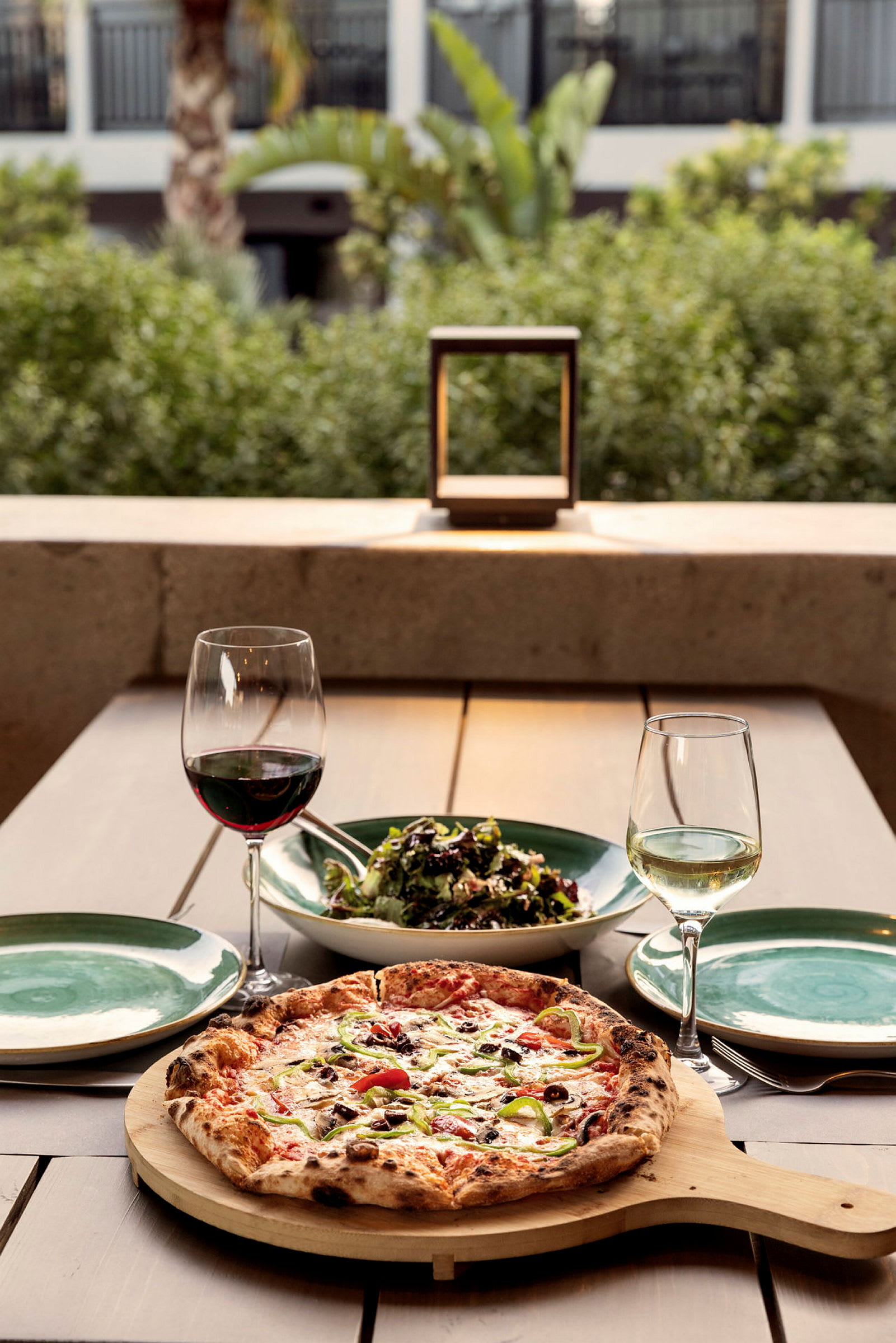 Et bord med en pizza, en bolle med salat, to vinglass og tallerkener. (AI-generert tekst)