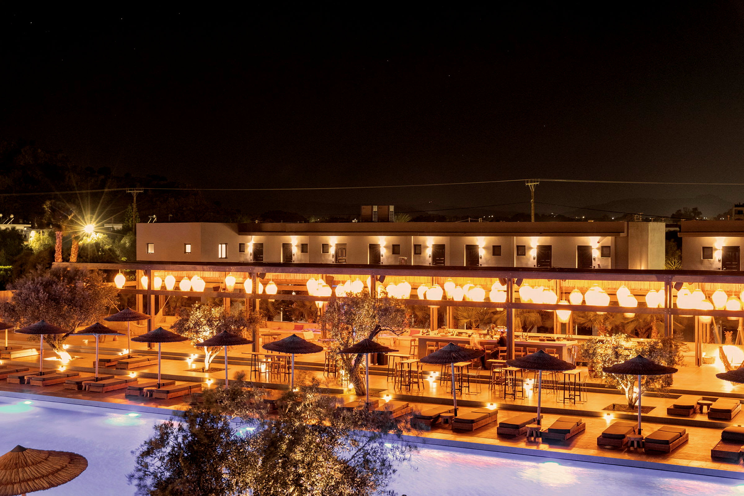 Nattbilde av en opplyst hotellterrasse med sitteplasser og et basseng. (AI-generert tekst)