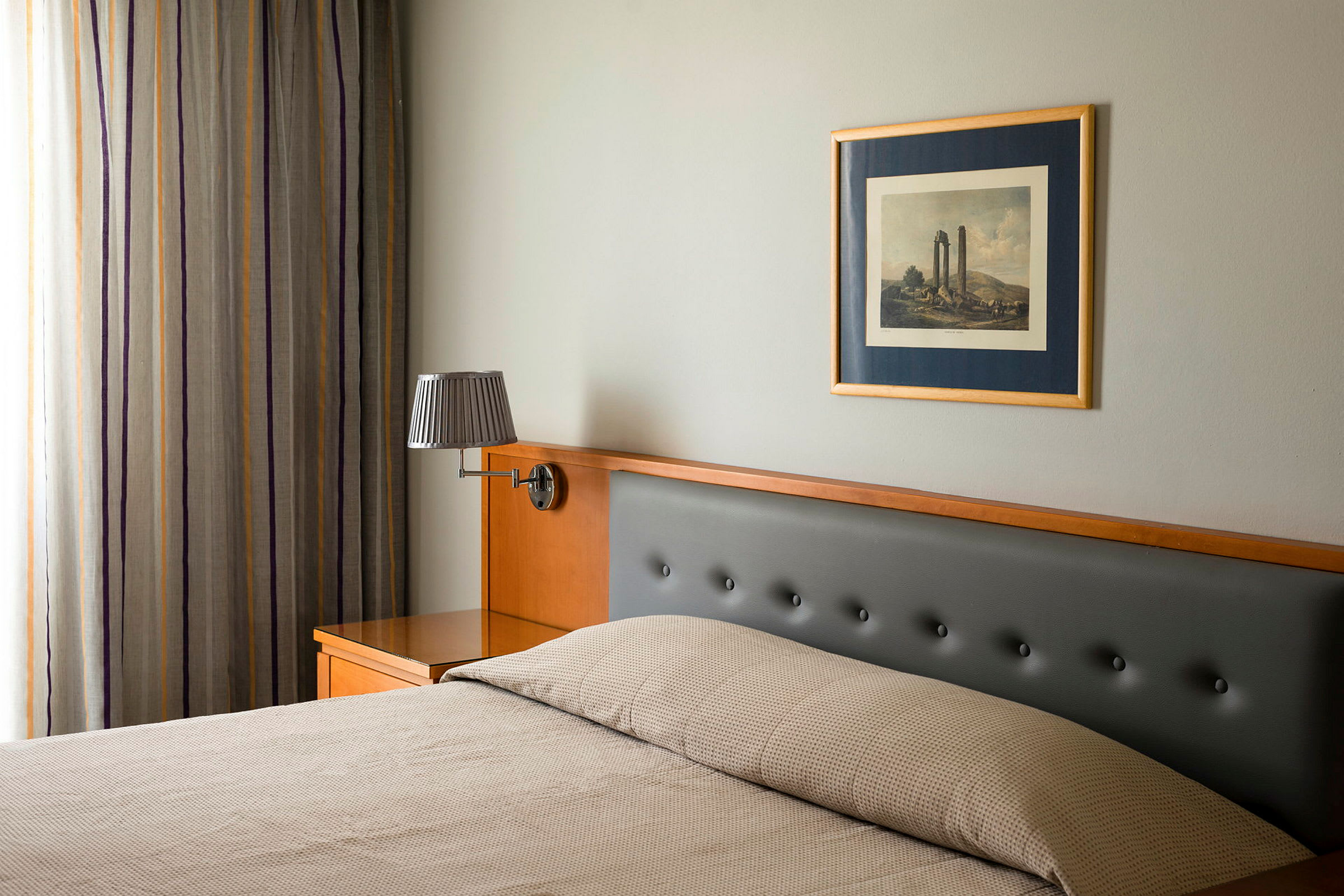 Et hotellrom med seng, vegglampe og bilde. (AI-generert tekst)