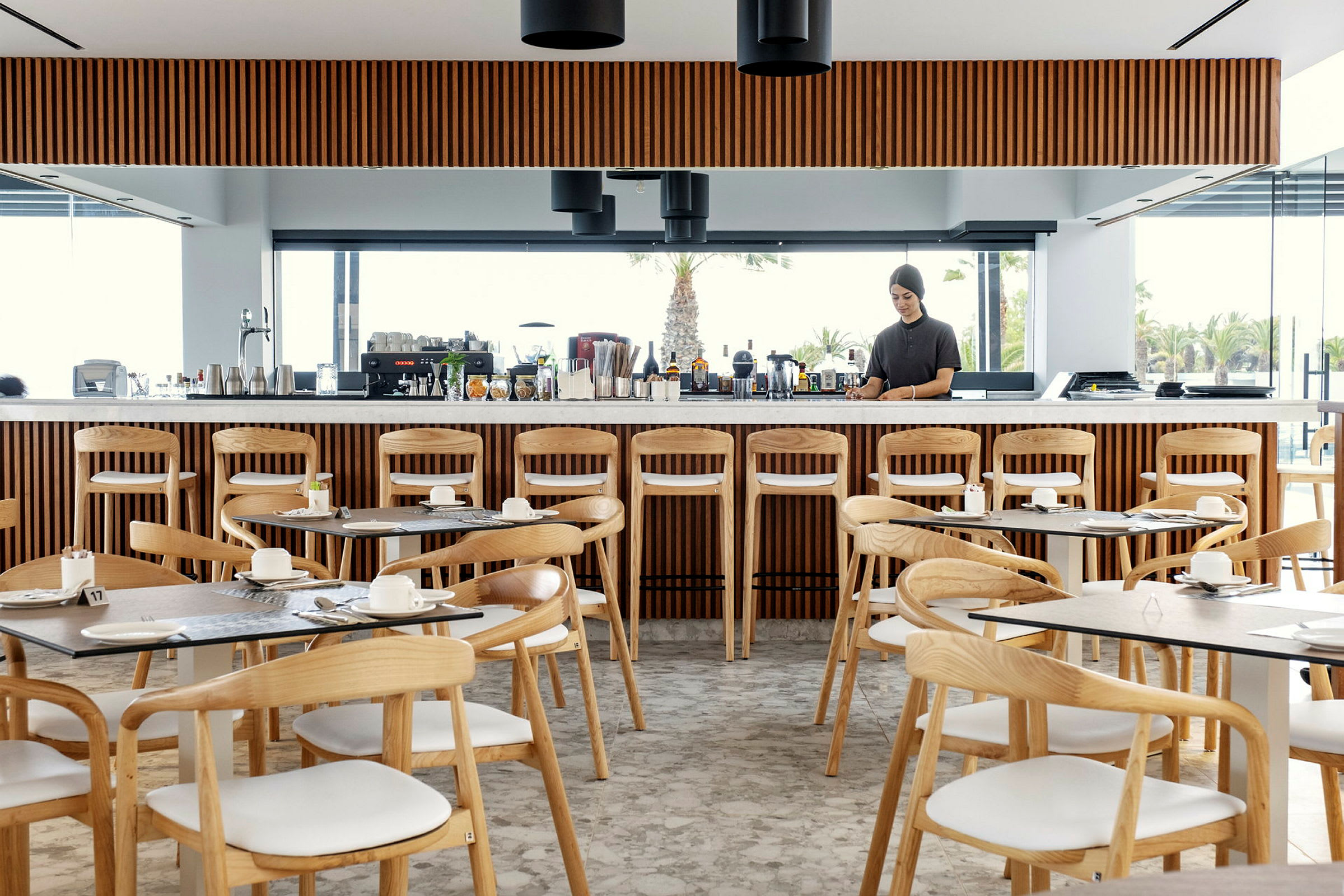 Restaurant med trestoler, bord og en lang bardisk med drikkevarer. (AI-generert tekst)