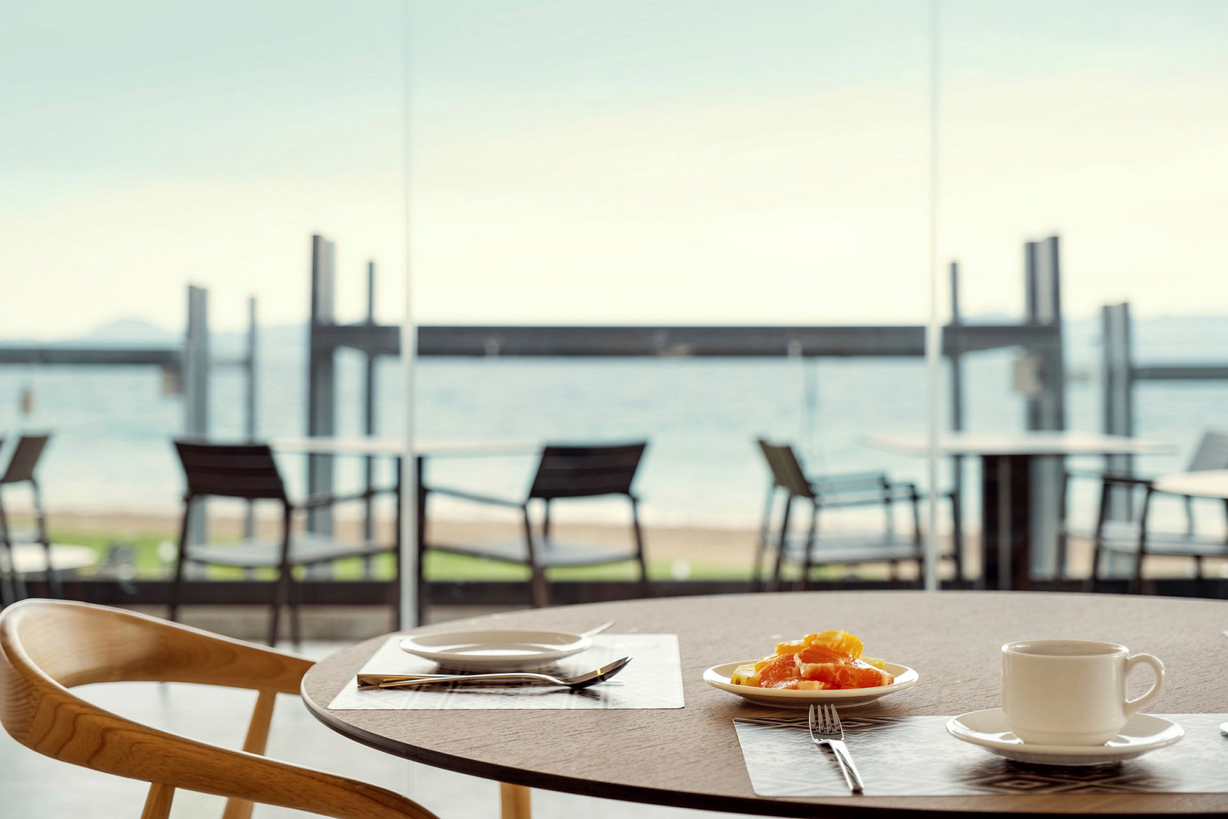 En tallerken med frukt og en kopp på et bord, med utsikt over stranden. (AI-generert tekst)