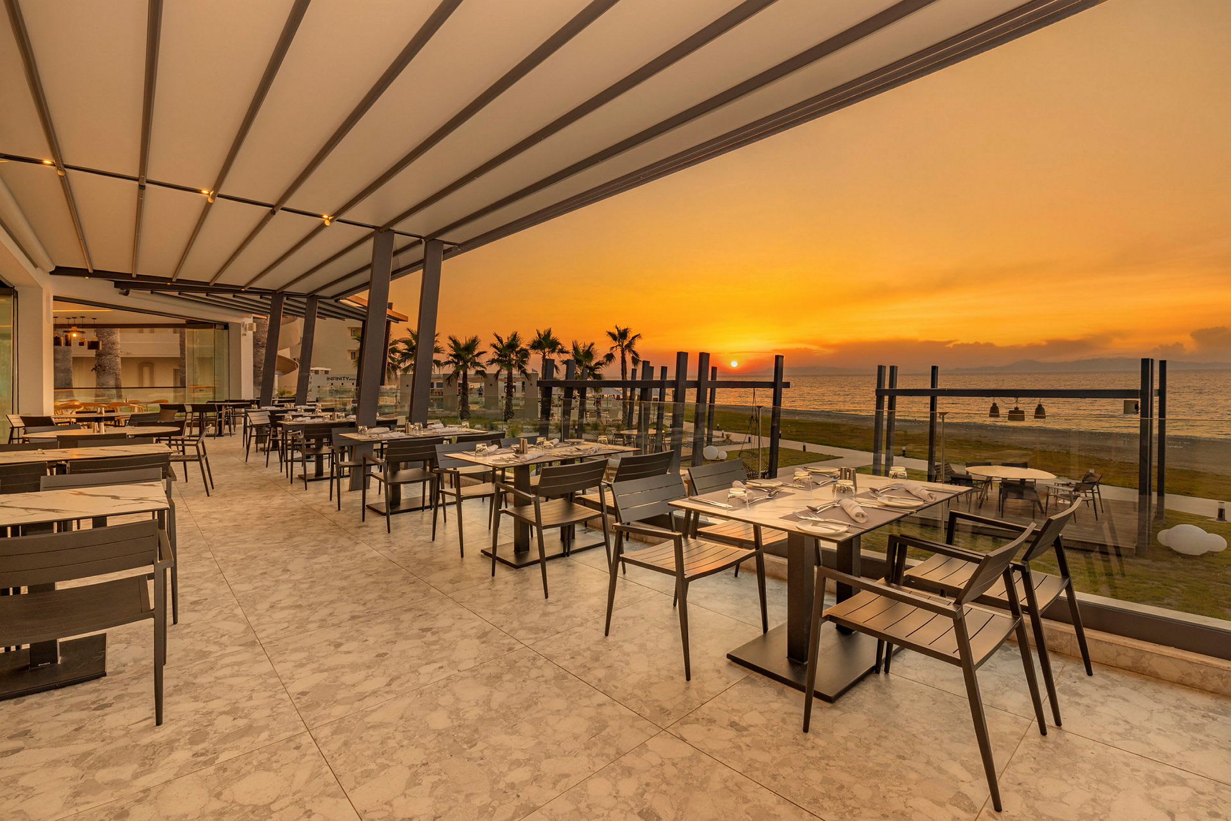 En utendørs restaurant med utsikt over havet ved solnedgang. (AI-generert tekst)