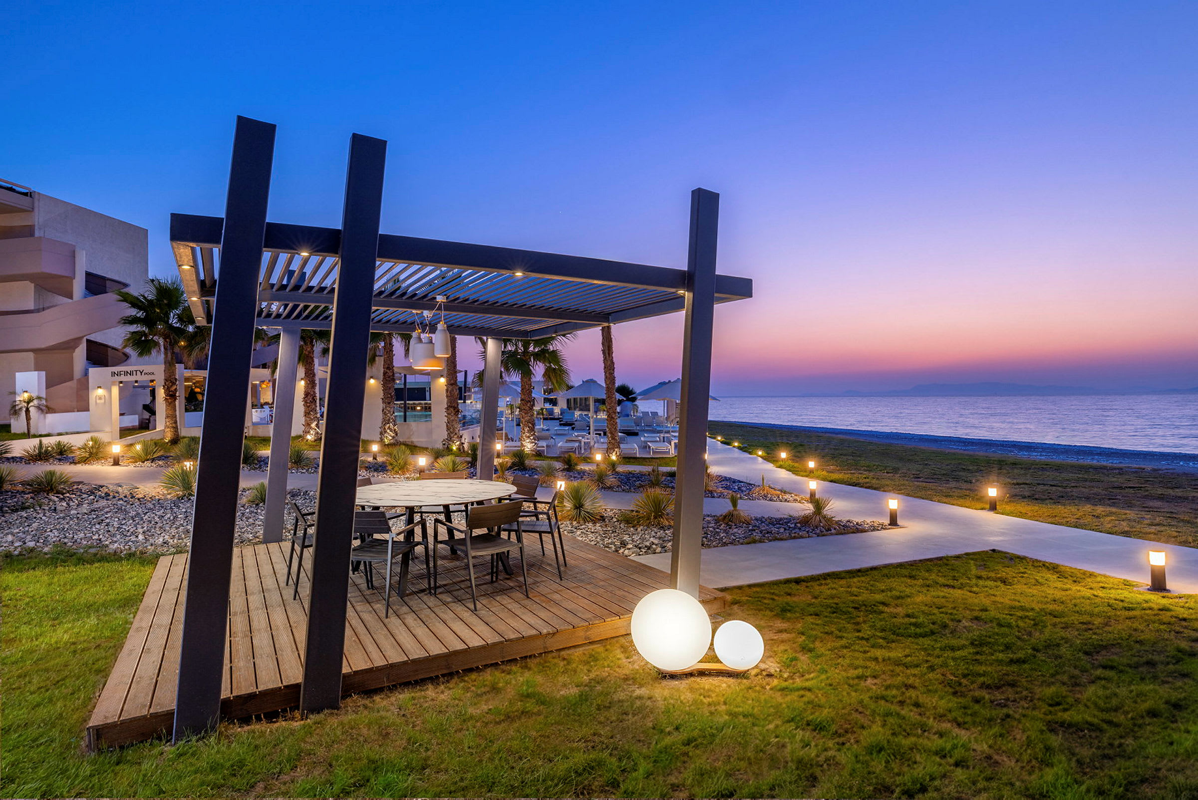 Et uteområde med et trebord under en pergola, med havutsikt i solnedgang. (AI-generert tekst)