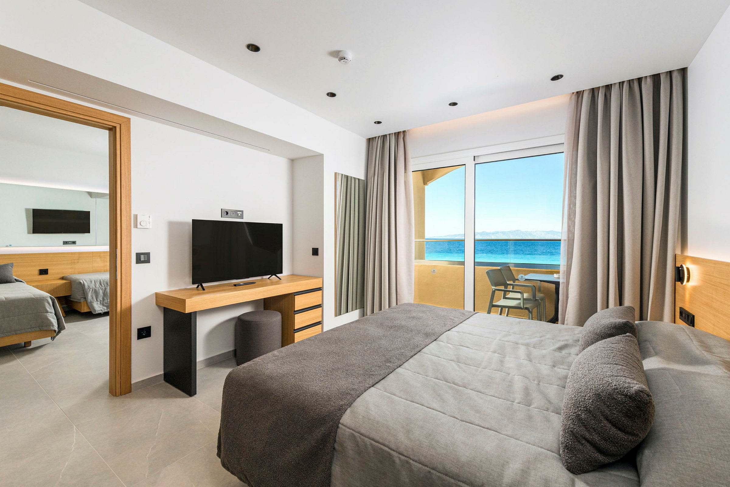 Hotellrom med moderne innredning, havutsikt gjennom glassdører og tilgang til balkong. (AI-generert tekst)