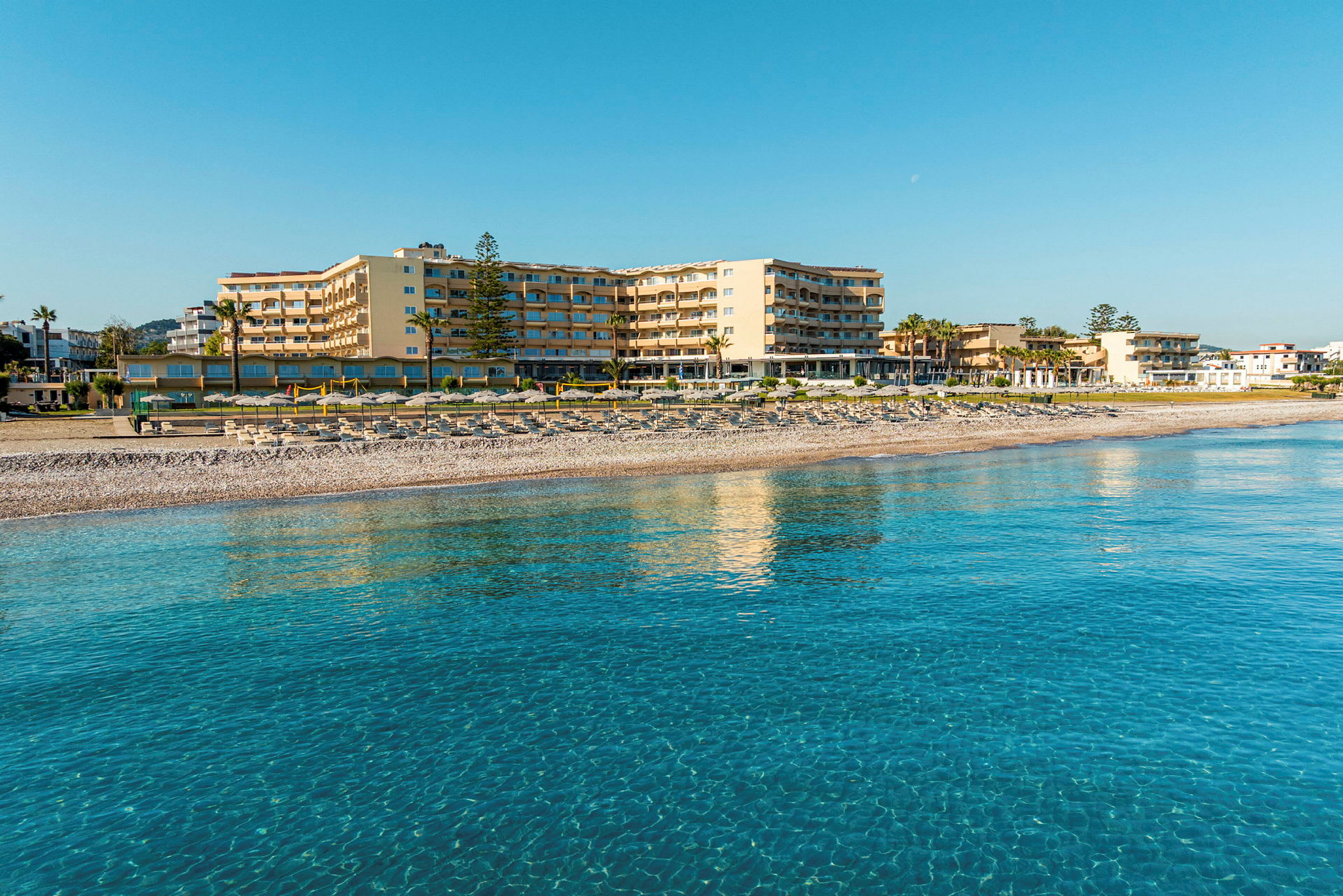 Et hotell ved stranden med klart blått vann i forgrunnen. (AI-generert tekst)