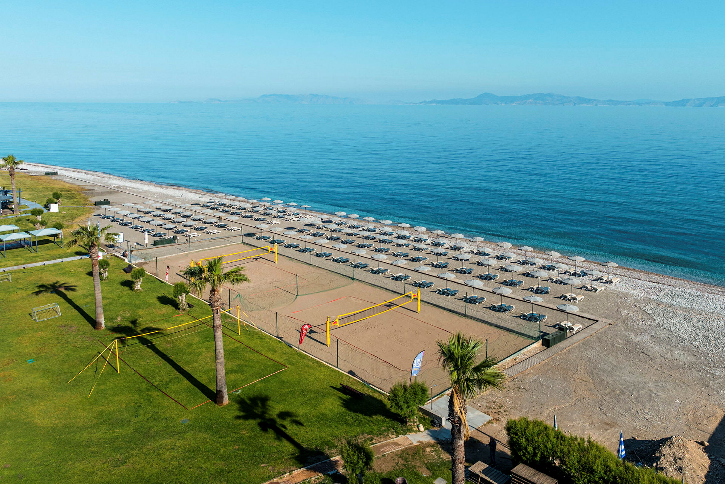 Bilde av en strand med solsenger og parasoller i flere rekker, en sandstrand og et volleyballnett ved siden av et grøntområde. (AI-generert tekst)