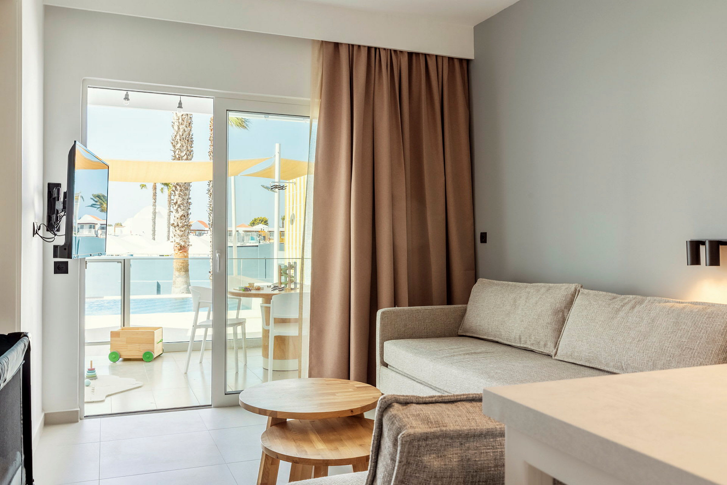 Stue med beige sofa og et trebord, samt glassdører som leder til en utendørsterrasse med møbler. (AI-generert tekst)